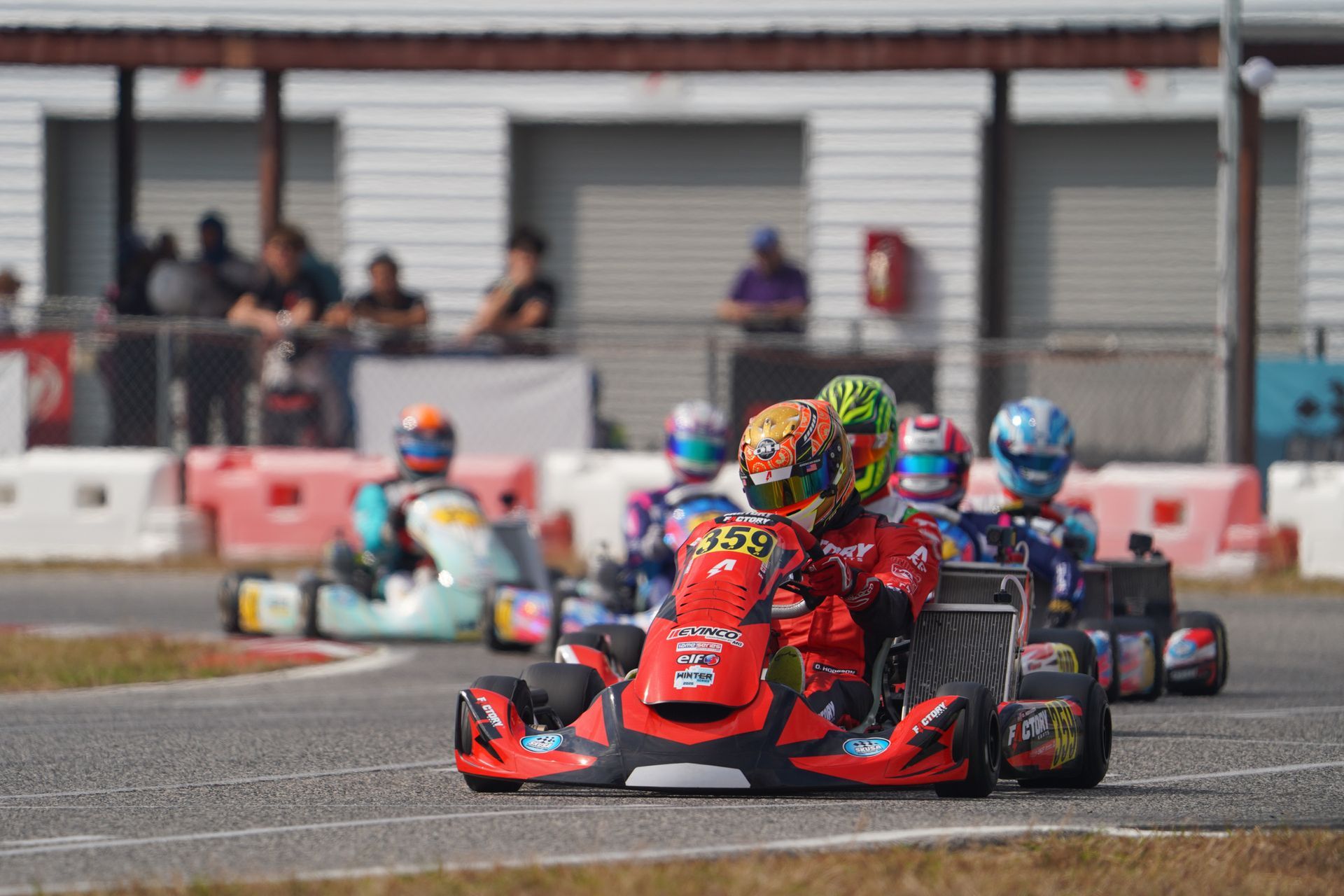 Go-kart race with two red karts leading on a track, spectators and barriers in the background