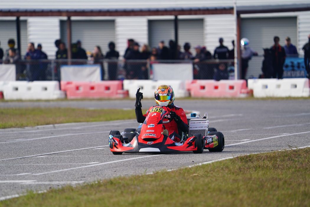 Red go-kart racing on a track with spectators watching behind barriers