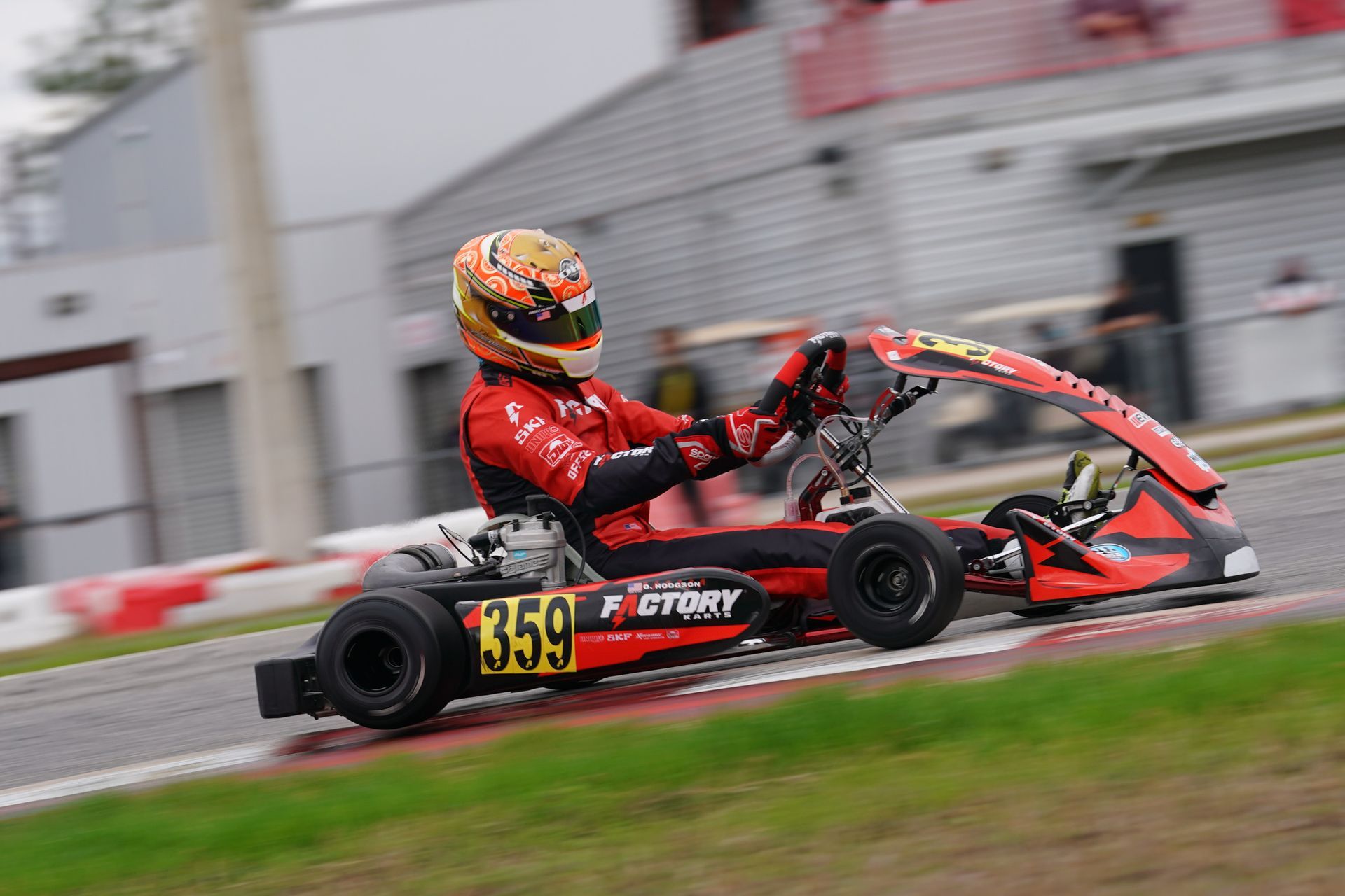 Go-kart racer in red suit and helmet speeding around a wet track, number 159 visible