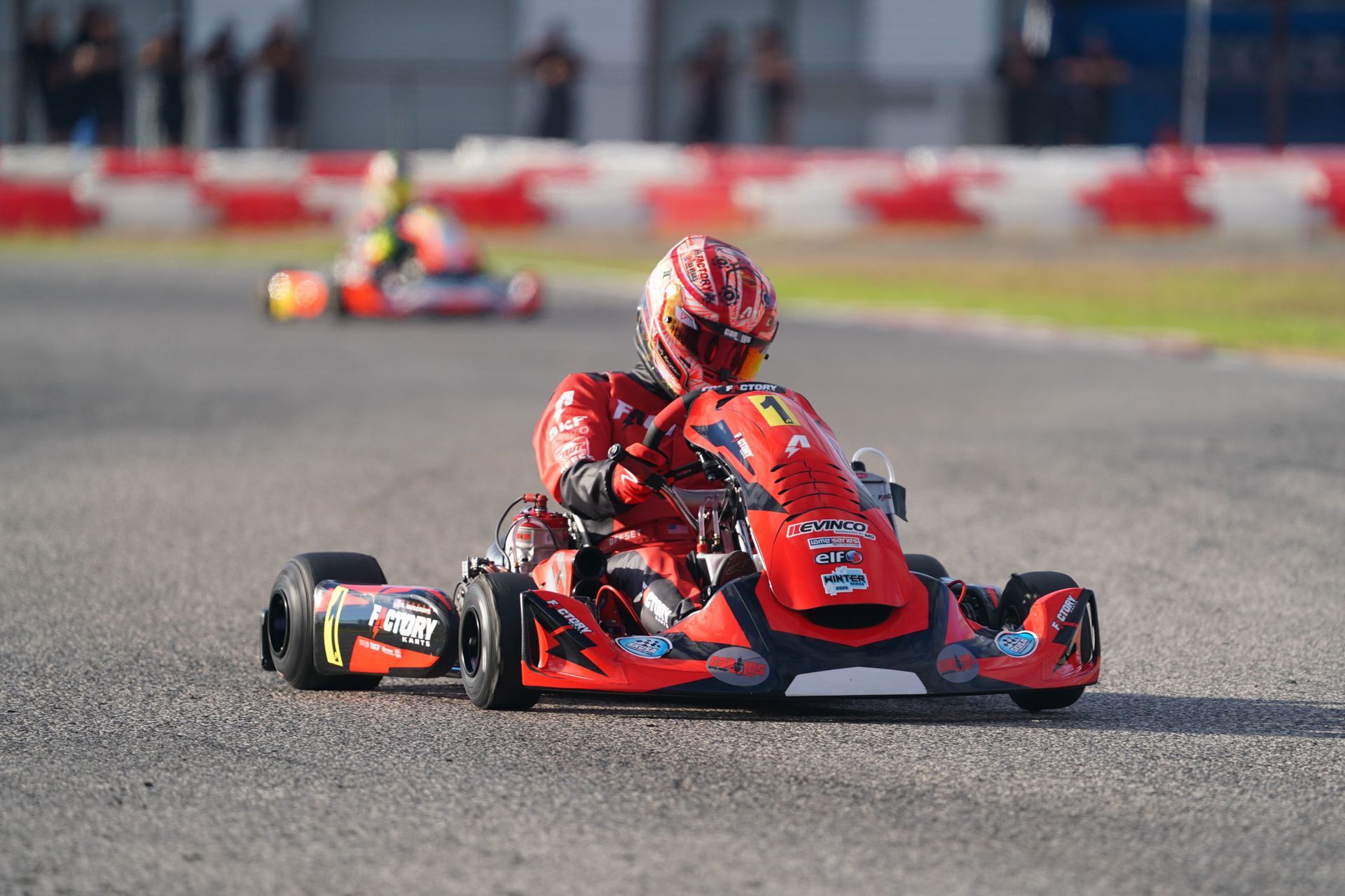 Red go-kart racing on a track, driver leaning into a turn with another kart blurred in the background