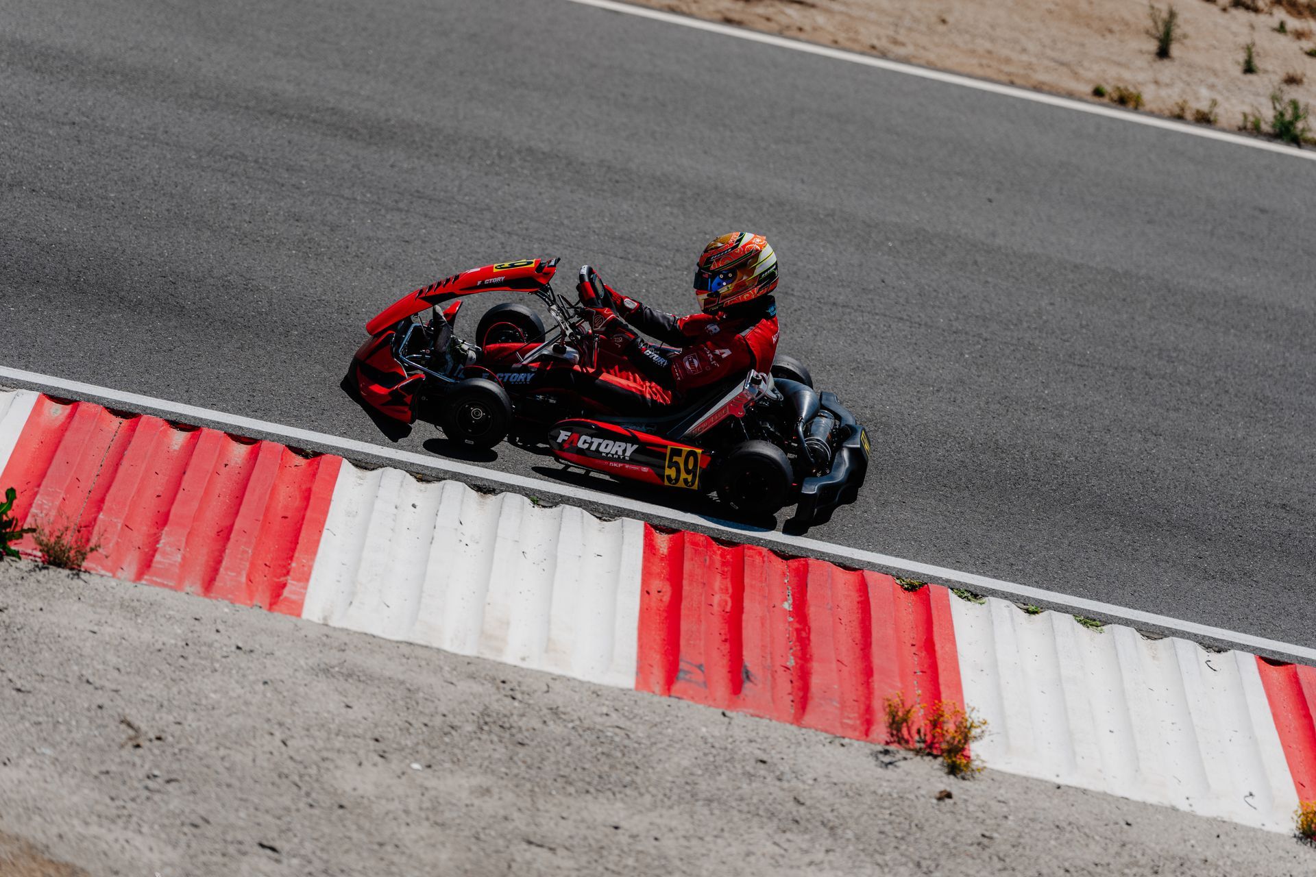 Red go-kart racer speeding on a wet track, wearing red gear and helmet, with blurred barriers behind.