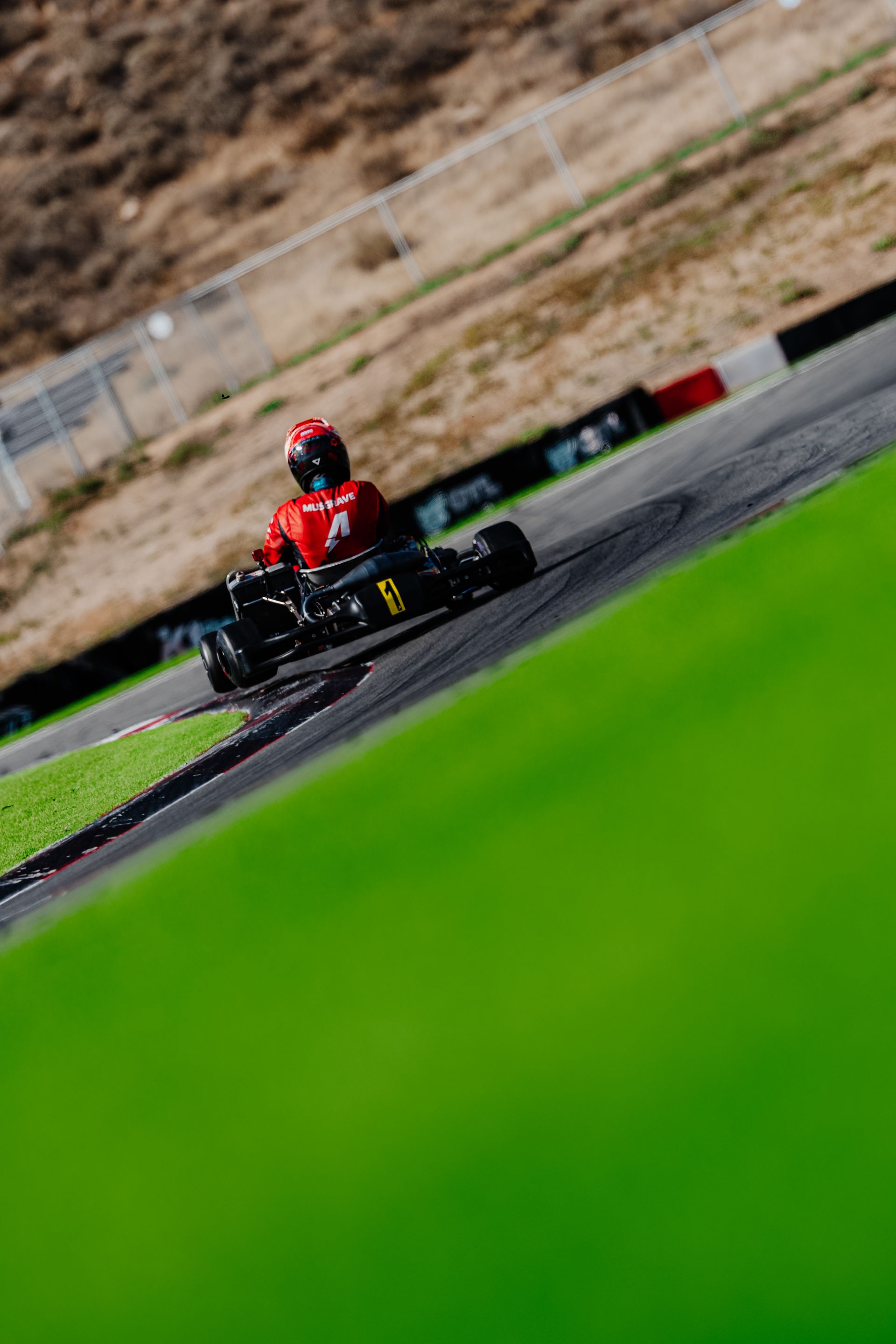 Red go-kart racing on a wet track, driver in a red helmet steering through a curve.
