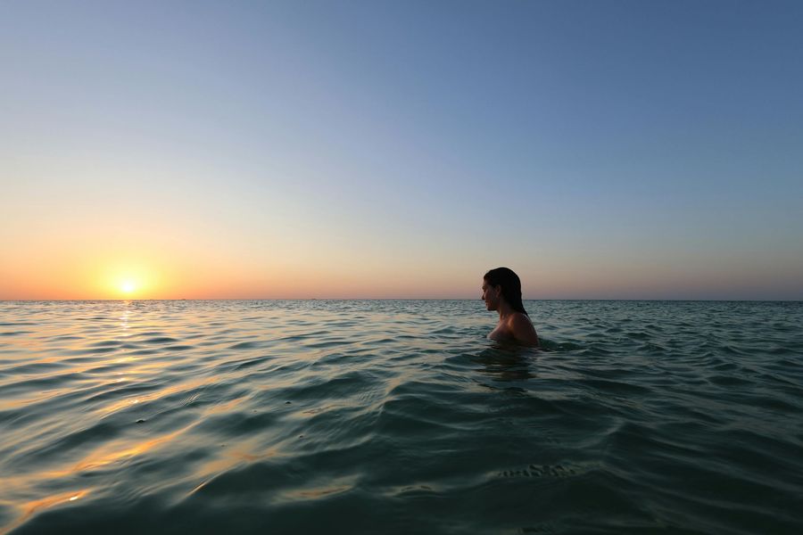 Person swimming in the ocean at sunset, with calm waves and a glowing horizon.