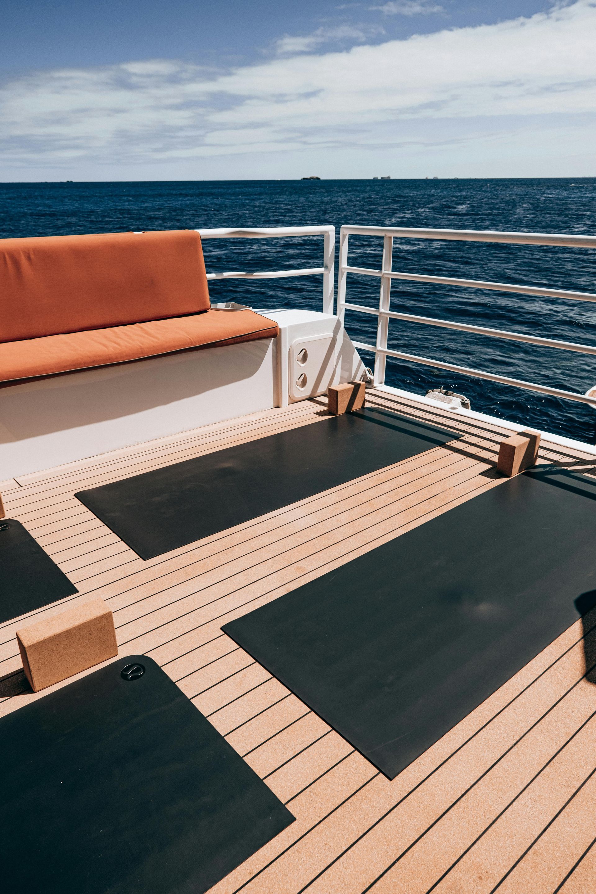 Boat deck with orange bench cushions, black mats, and ocean view under a cloudy sky