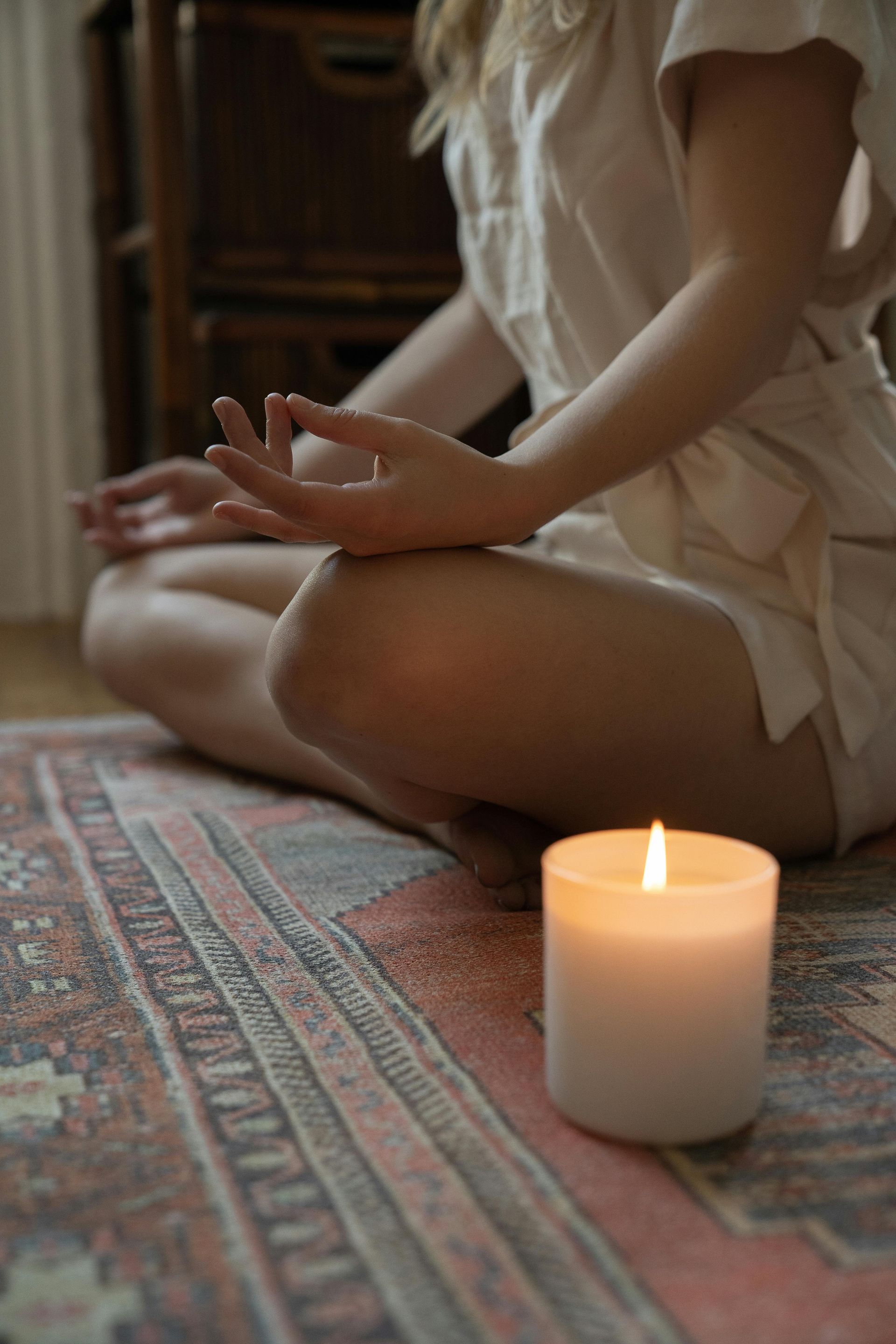Person sitting cross-legged on a rug beside a lit candle in a softly lit room