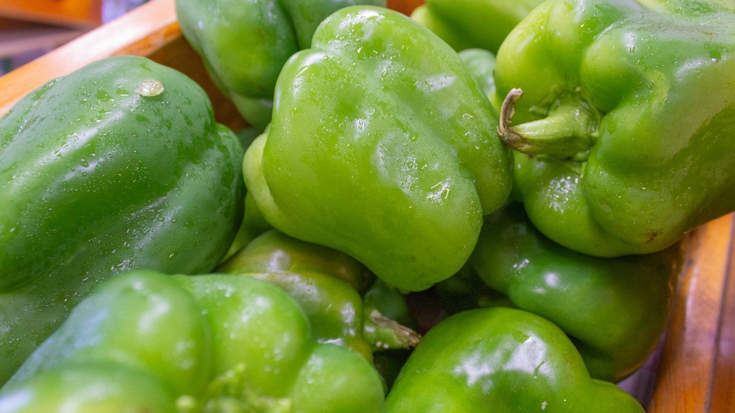 A bunch of green peppers are sitting in a wooden bowl.