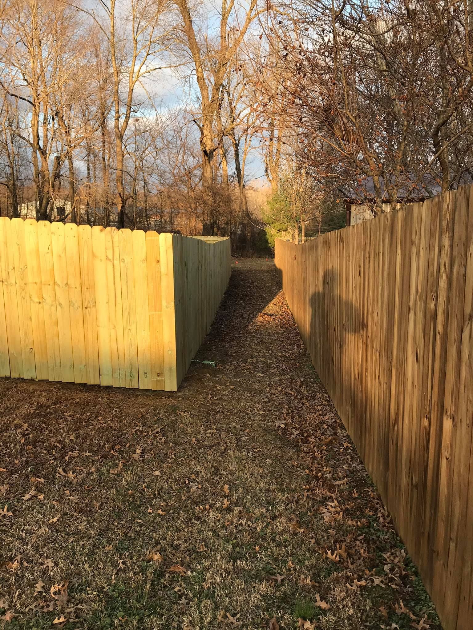 A wooden fence along a path surrounded by trees.