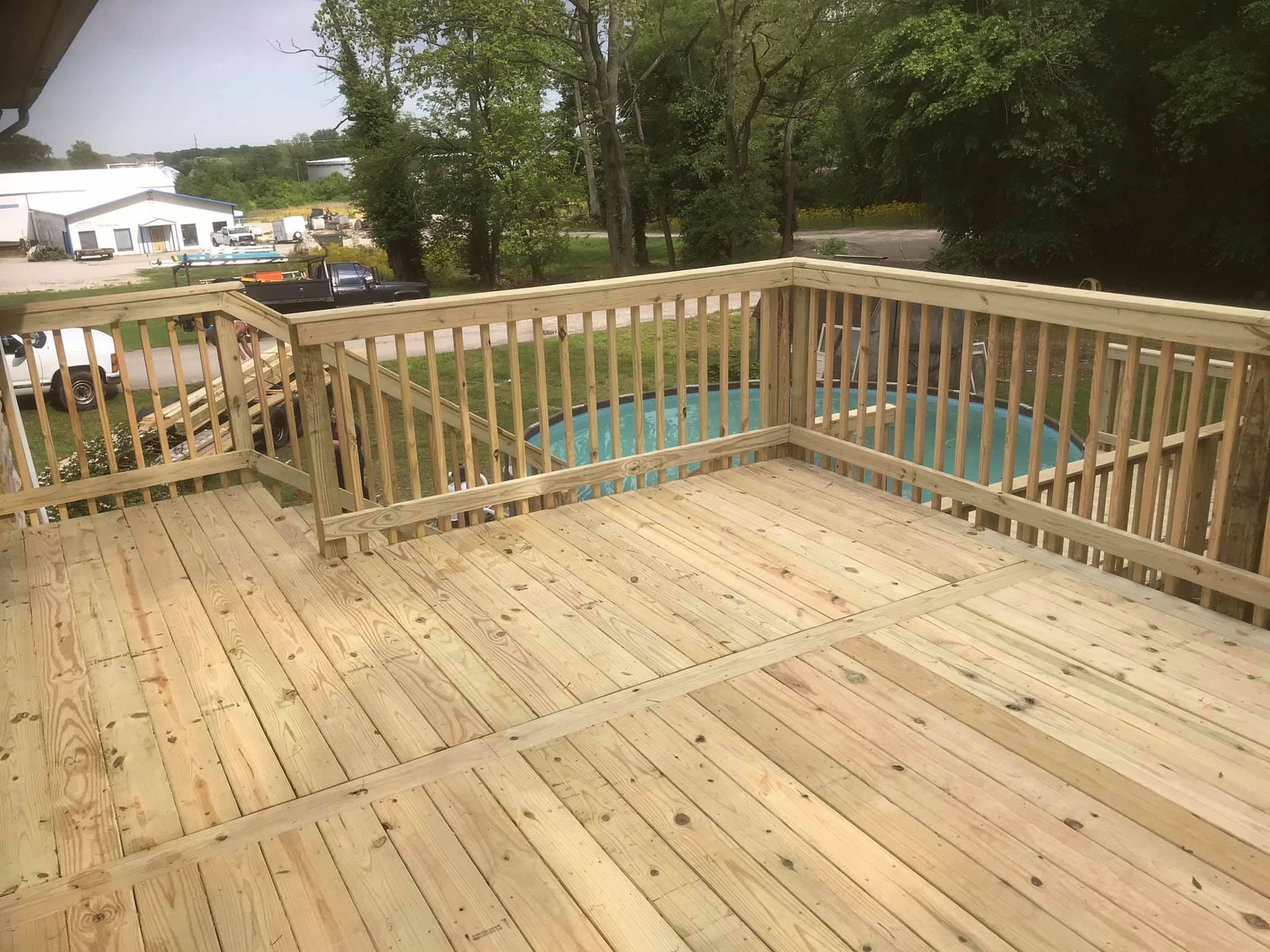 A large wooden deck with stairs and a pool in the background.