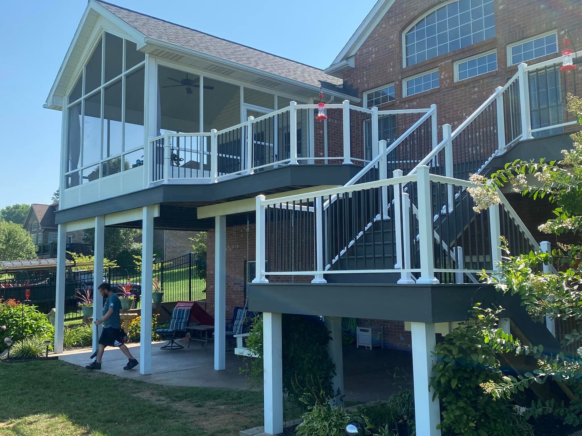 A man is walking in front of a house with a screened in porch and stairs.