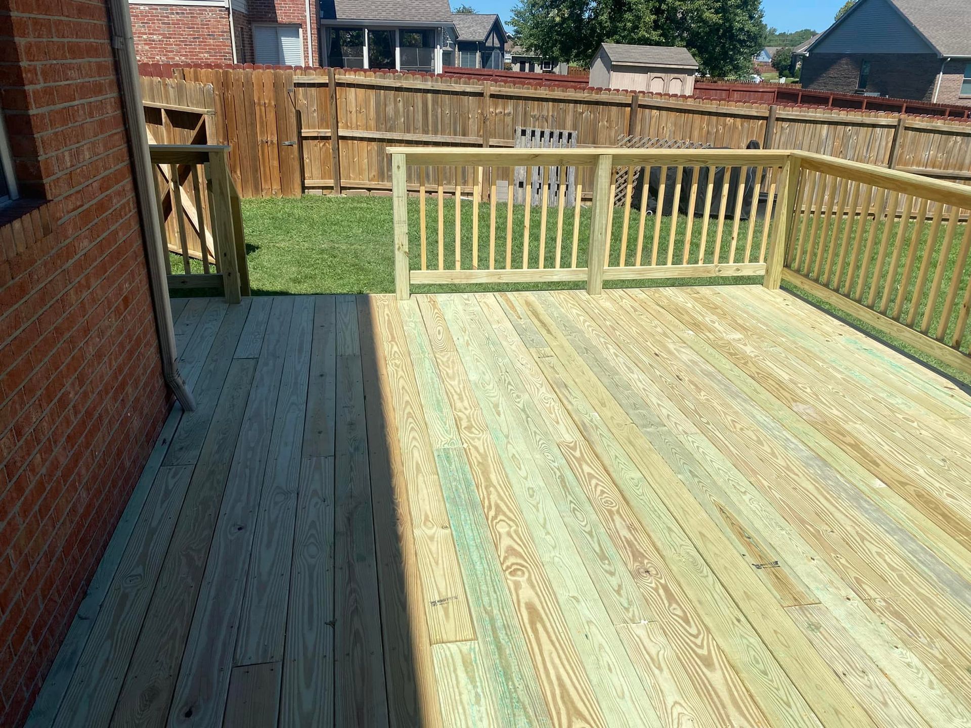 A wooden deck with a railing in the backyard of a house.