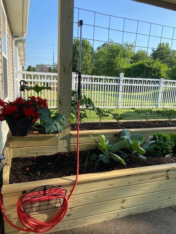 A wooden garden bed with a red hose attached to it.