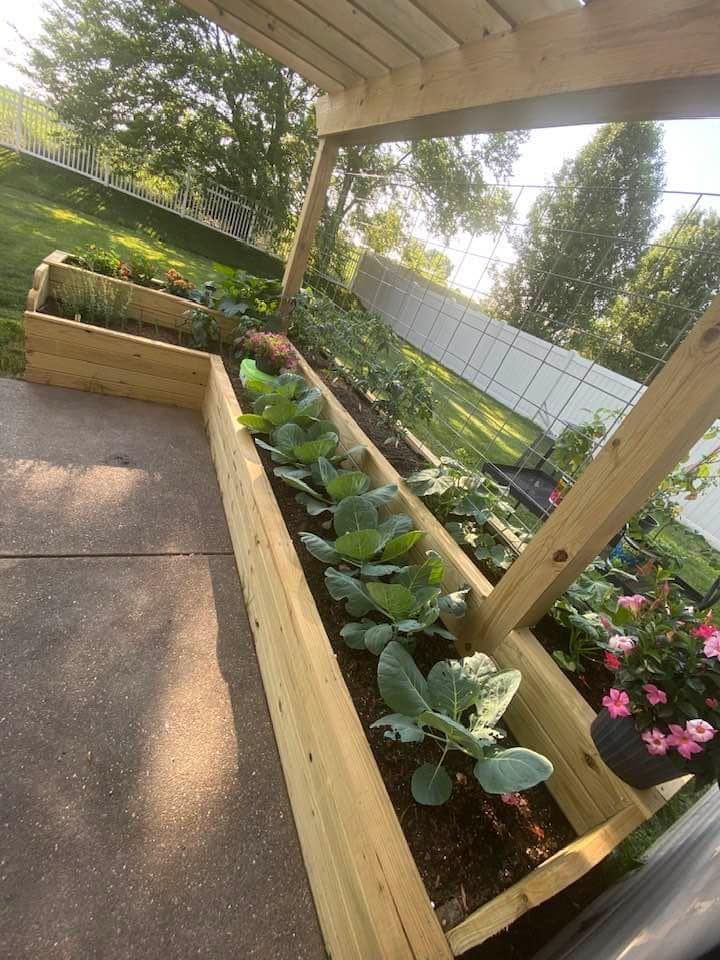 A wooden planter filled with vegetables and flowers on a patio.