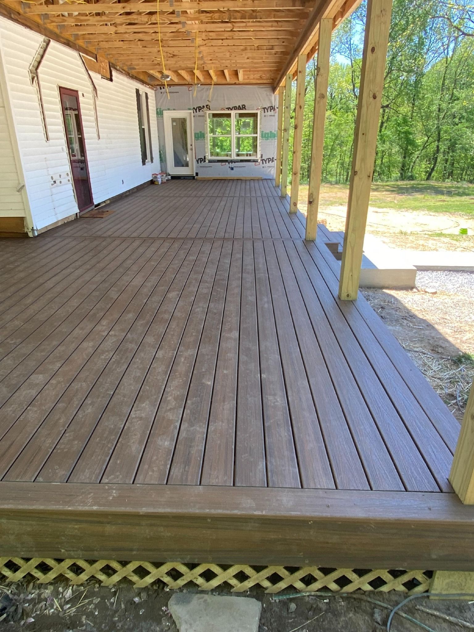 A large wooden deck with a covered porch and a white house in the background.