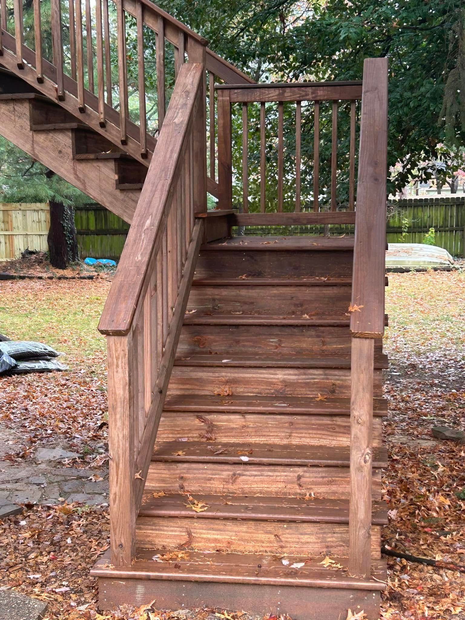 A wooden staircase leading up to a deck with leaves on the ground.