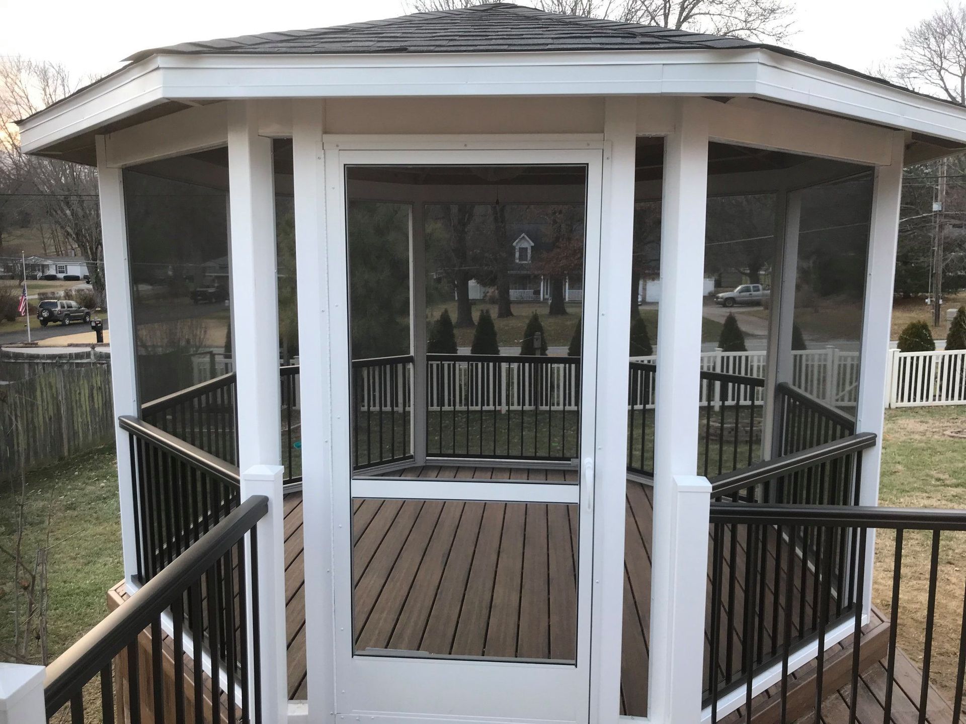 White gazebo with a wraparound railing and dark wooden floor on a lakeside dock