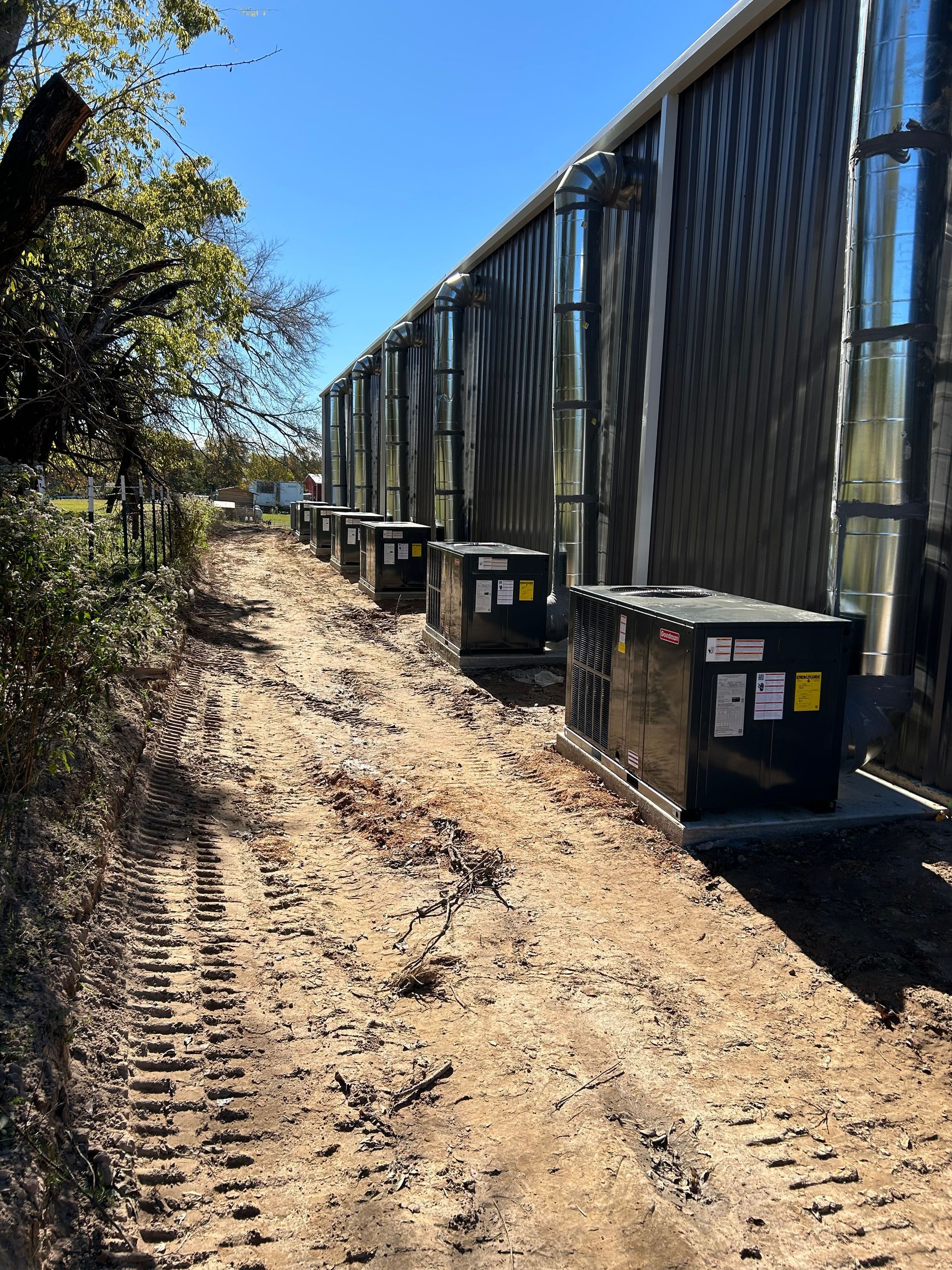 Exterior view of a building with air conditioning units lined up along a dirt path.