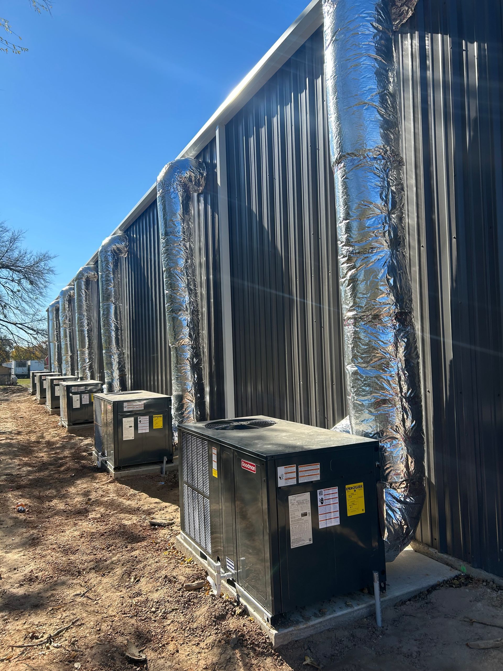 Row of large air conditioning units outside a building with metal siding and insulated ductwork.