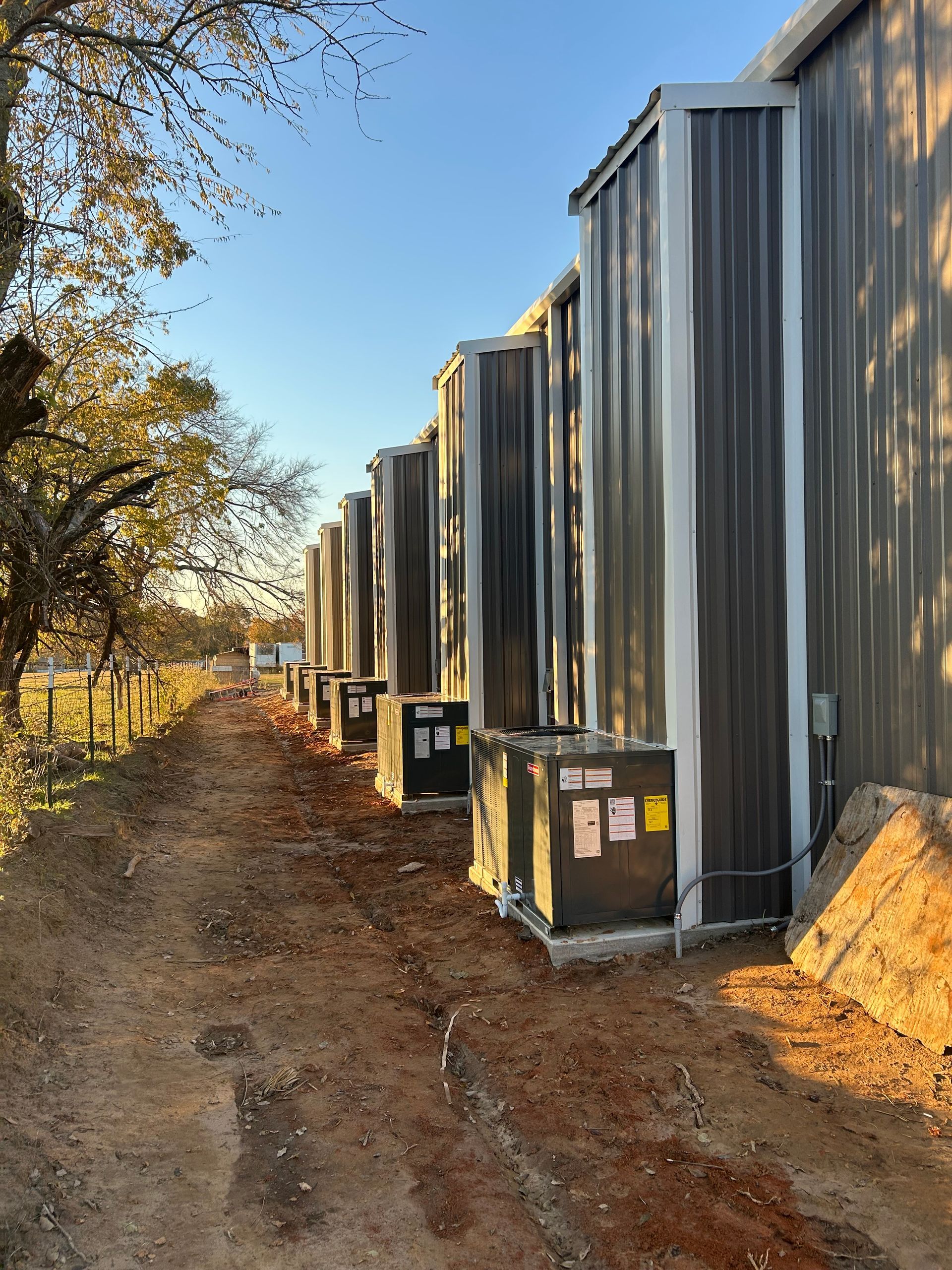 Row of metal-clad units with air conditioning units lined along a dirt path.