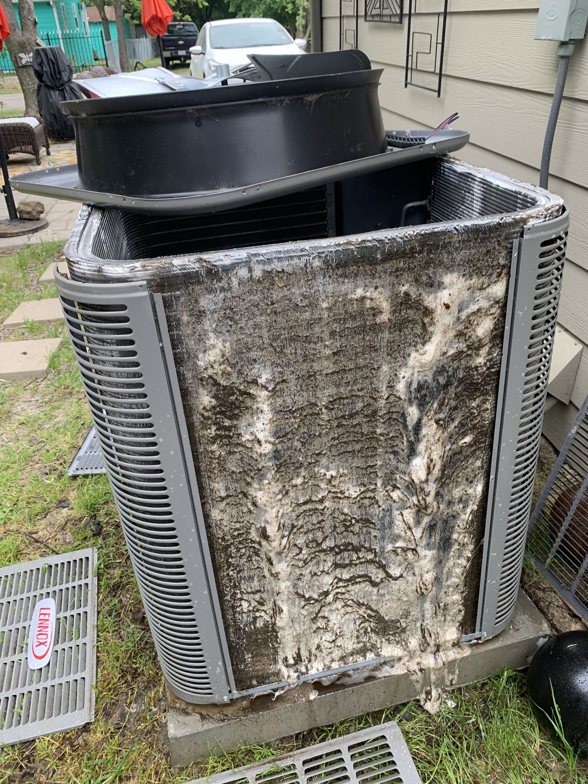 Air conditioner unit with dirty coils, top removed, sitting outdoors.