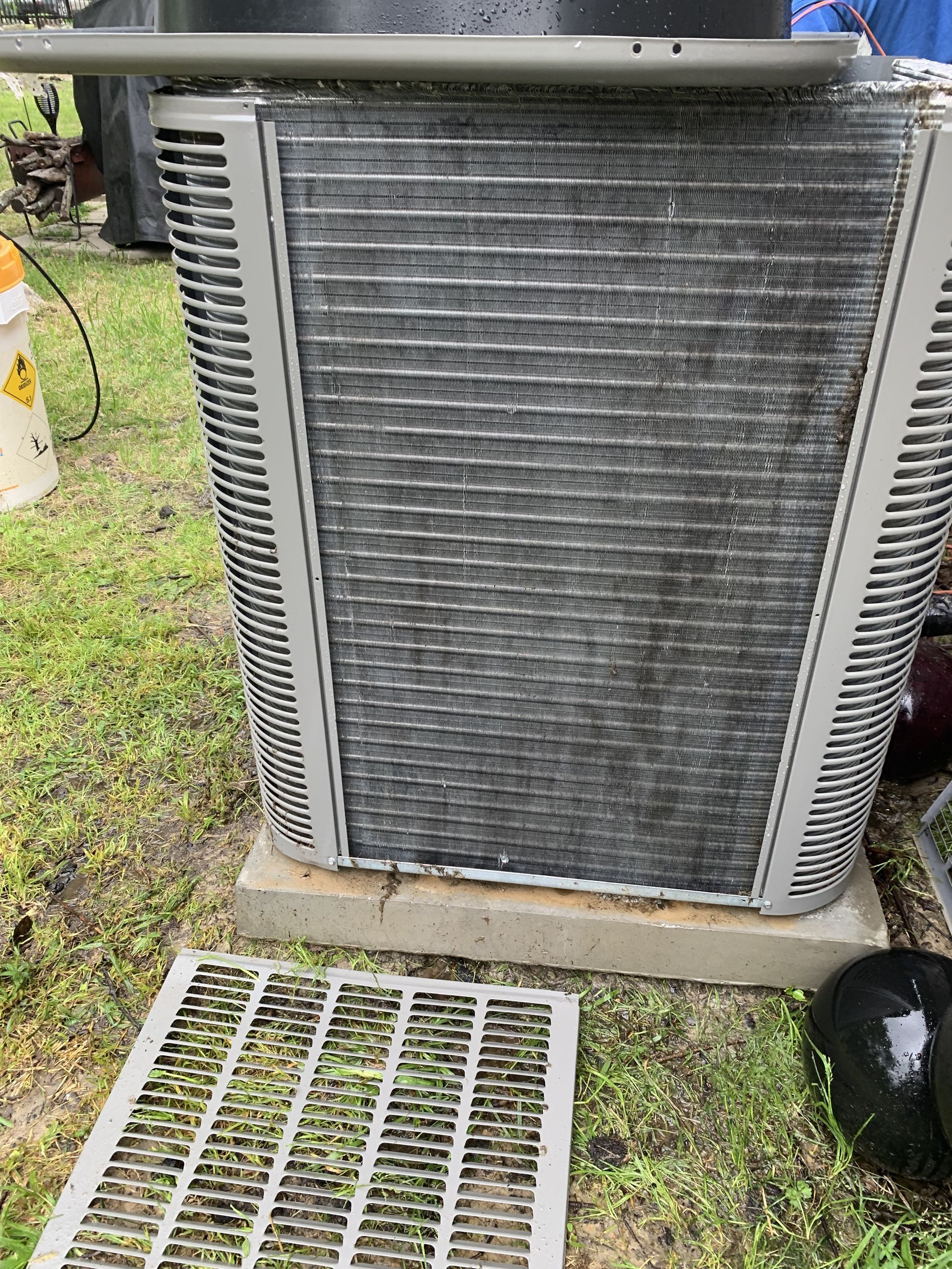 Outdoor air conditioner unit, metal fins, gray frame, sitting on a concrete base, with a removed screen on the grass.