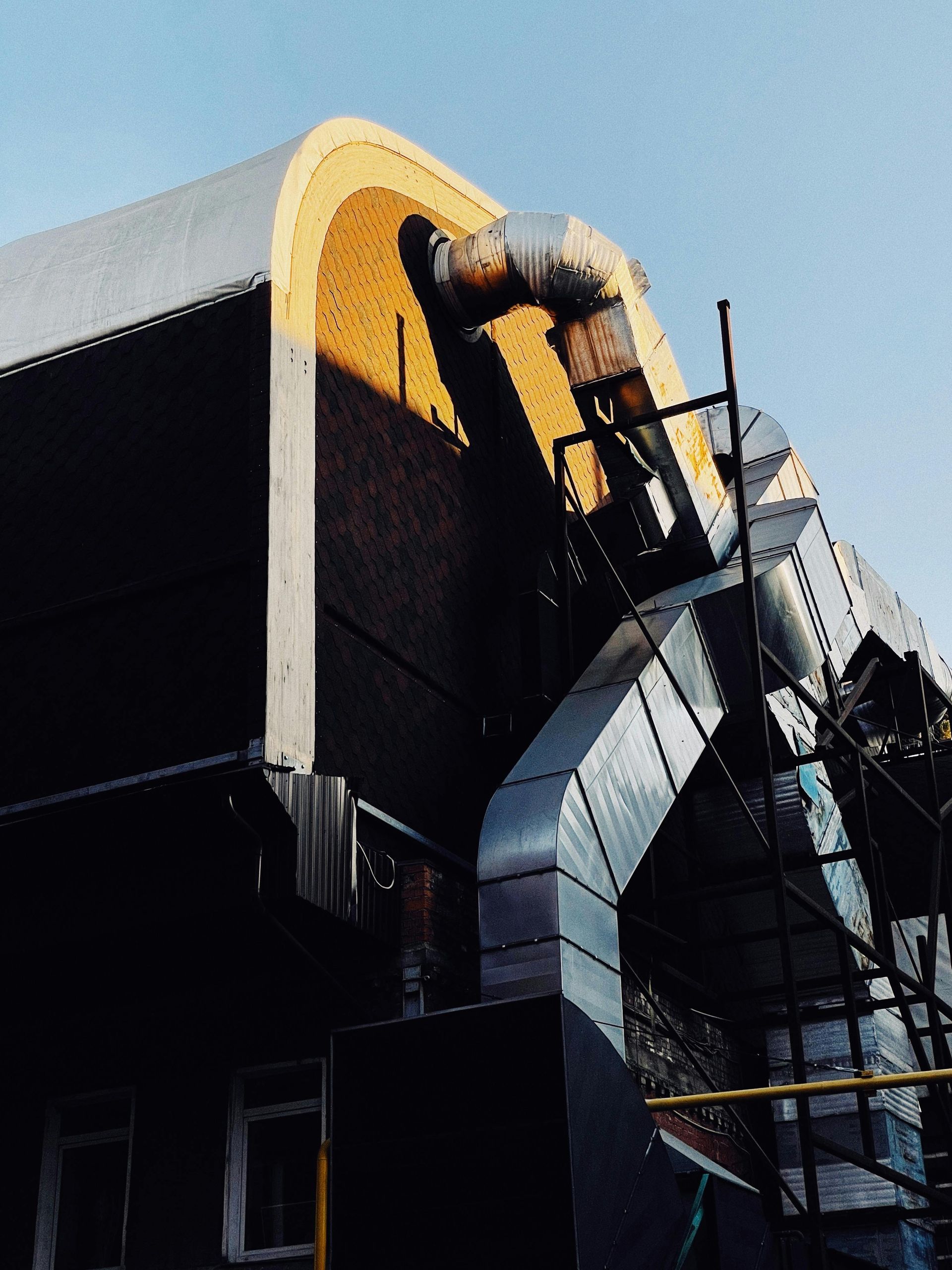Industrial building exterior with curved roof, ductwork, scaffolding, and insulated walls.