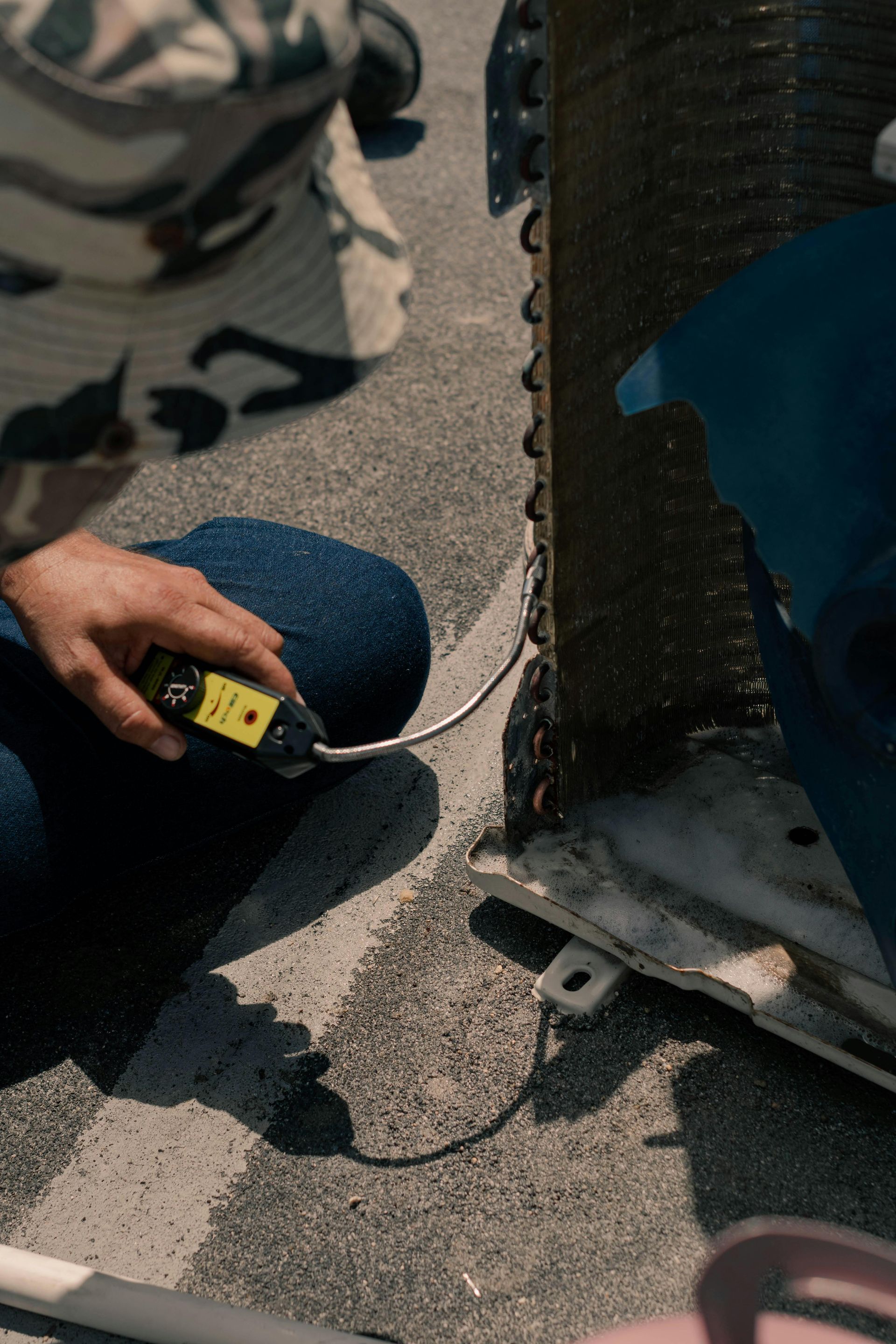Person in blue jeans using a device near a metal cylinder on a gray surface, likely an inspection.
