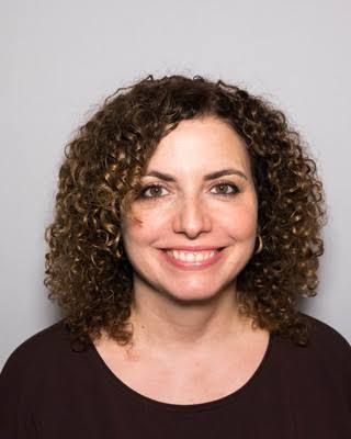 Smiling woman with curly dark hair against a light gray background