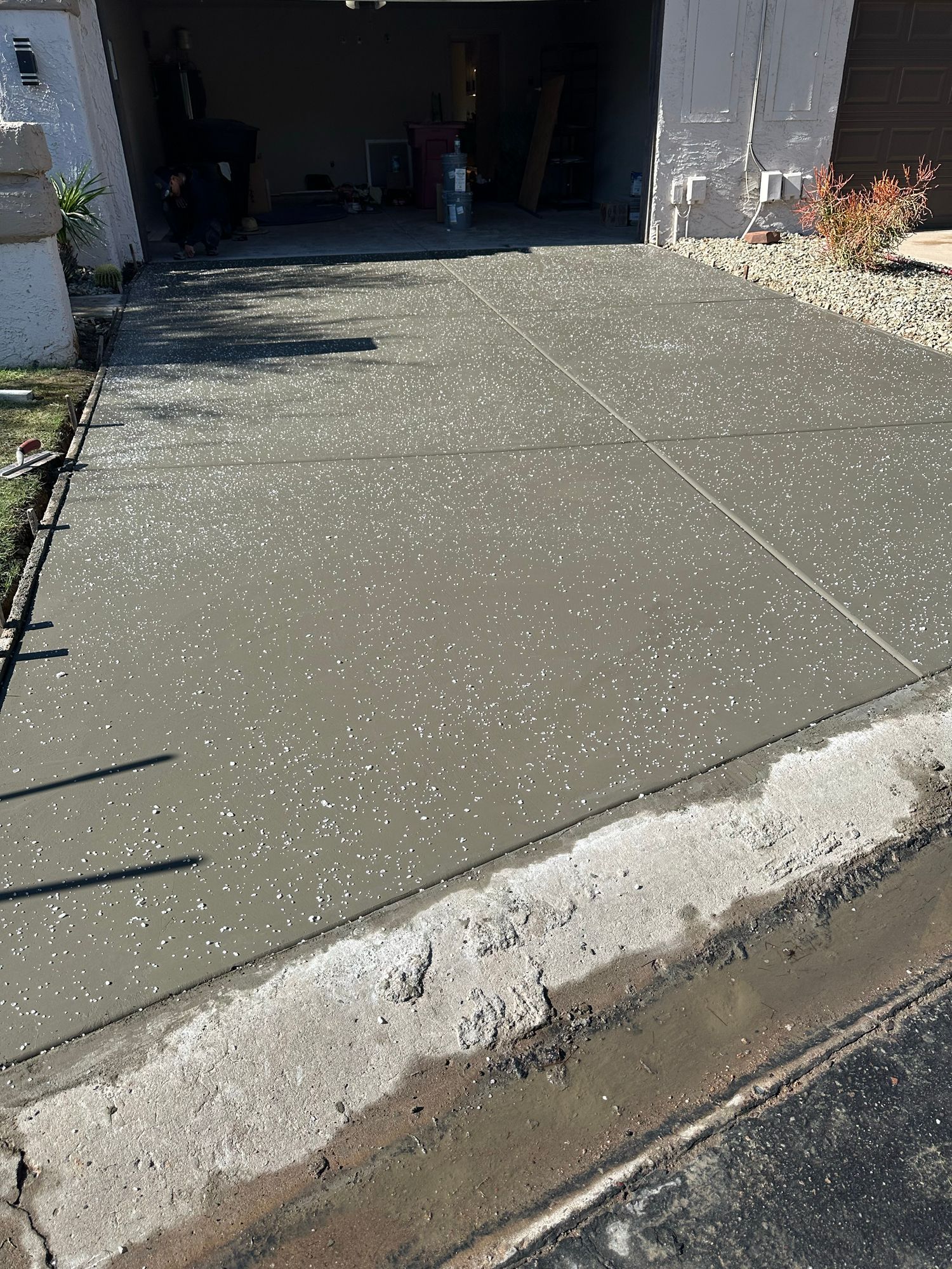 A freshly poured grey concrete driveway in front of a garage, covered in a light dusting of hail or white debris.