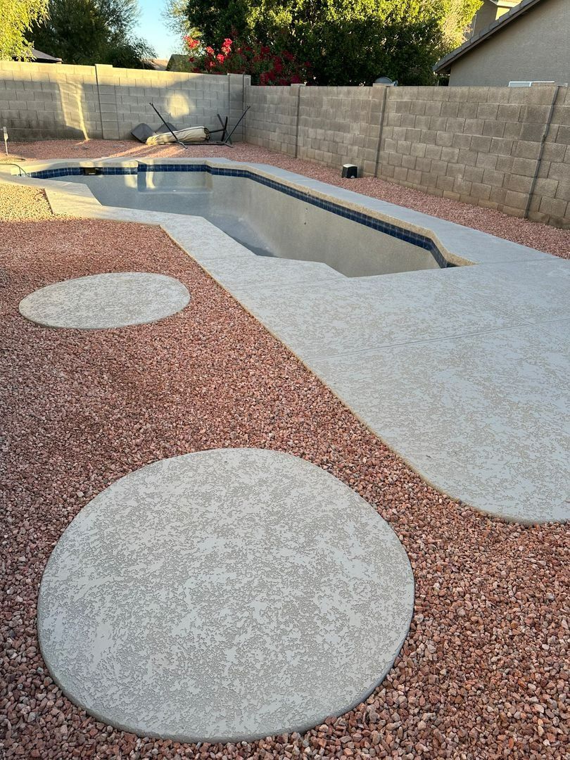 A swimming pool surrounded by a concrete deck and decorative reddish-brown gravel, featuring two circular concrete pads.
