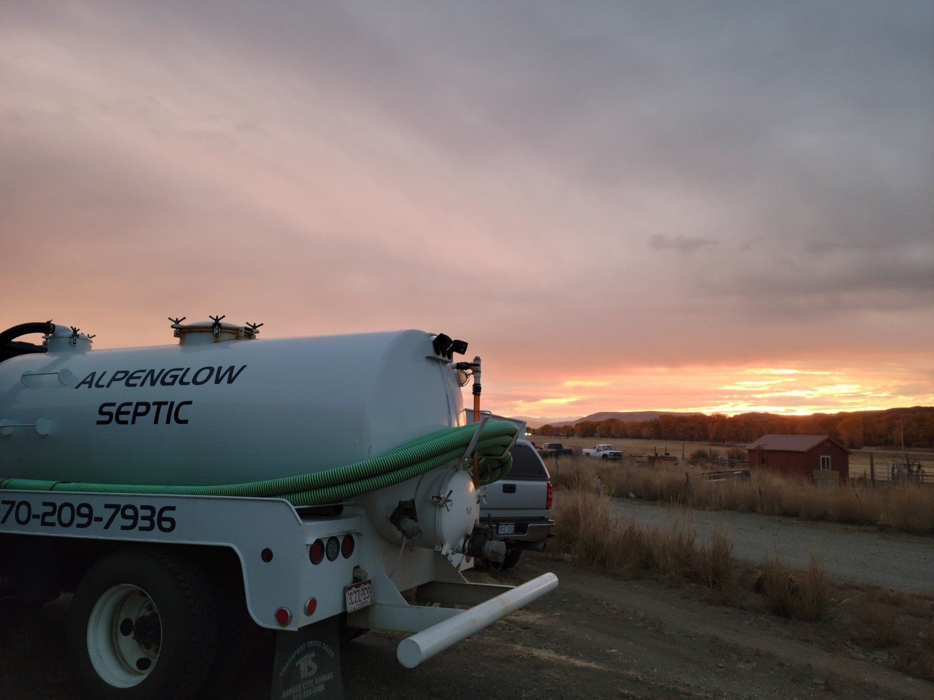 Septic service truck at sunset in a field, with a hose extending from the tank.
