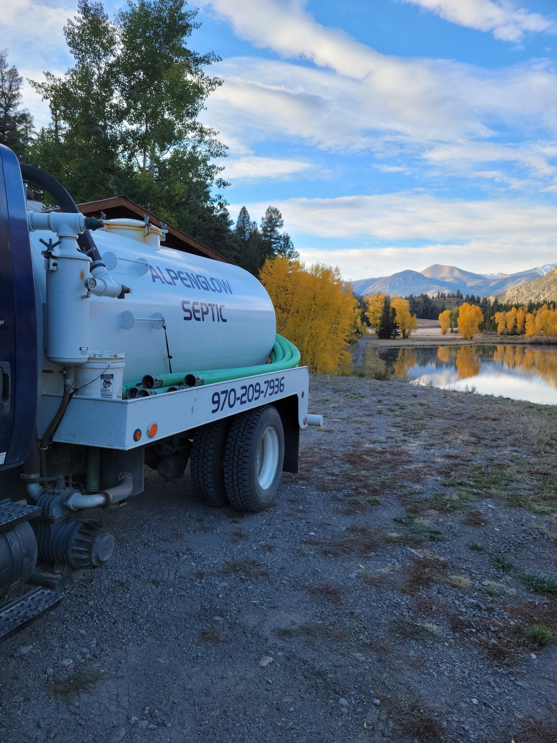 White utility truck by a river with autumn trees and mountains in the background