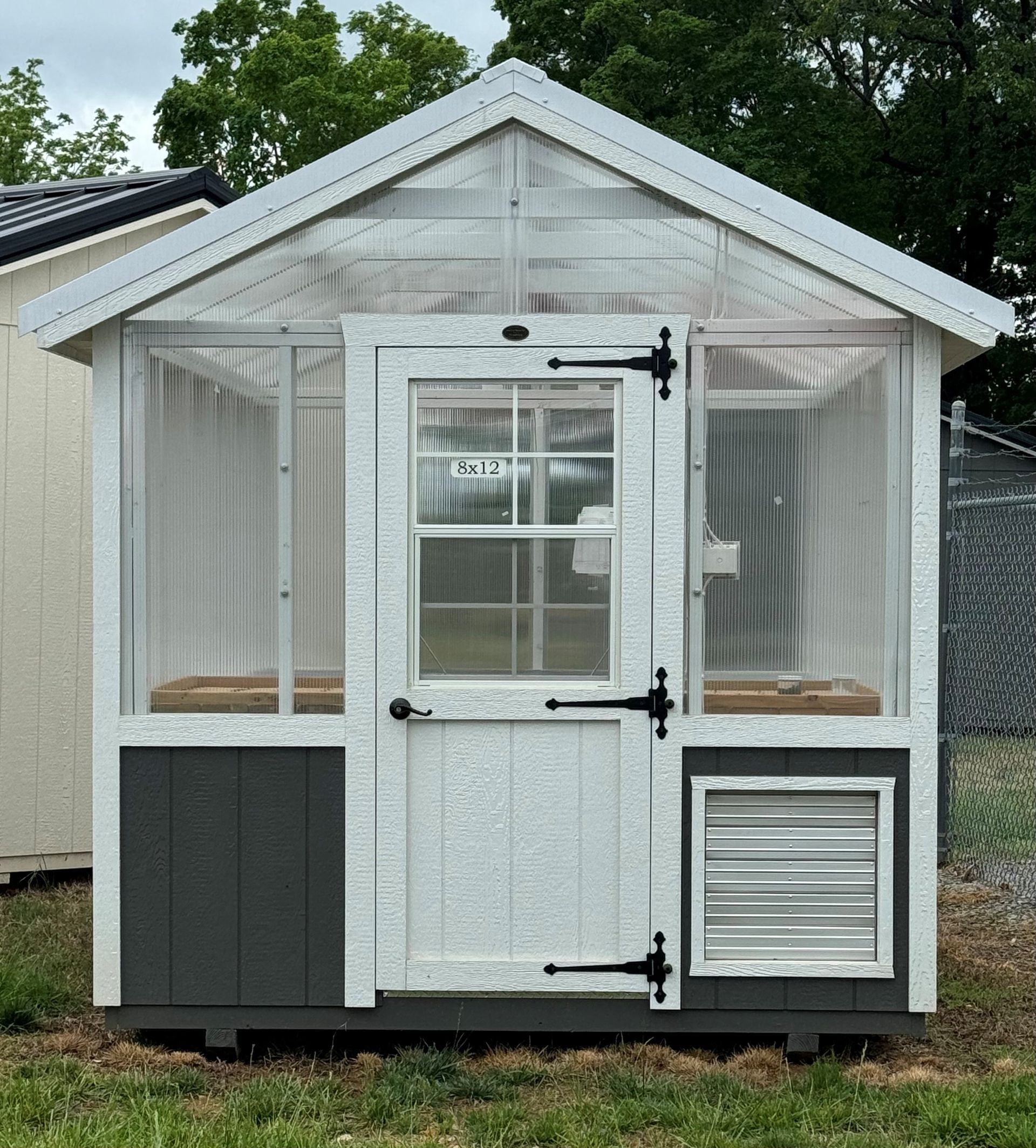 Small white-and-gray garden shed with front windows, a centered door, and louvered vent panels.