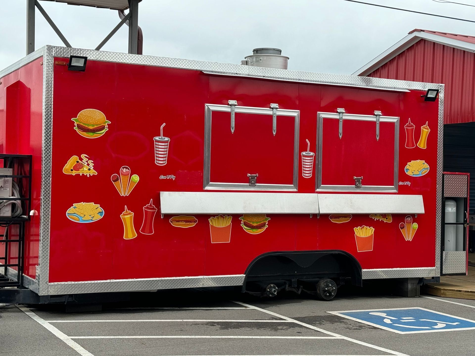 Red food truck with serving windows and burger, fries, and drink graphics parked in a lot.
