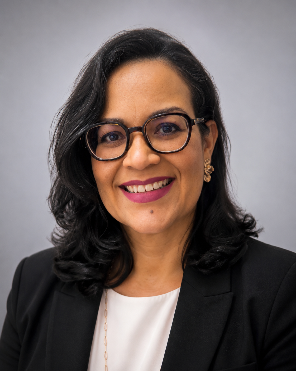 Portrait of a smiling woman in glasses, black blazer, and white top against a gray background
