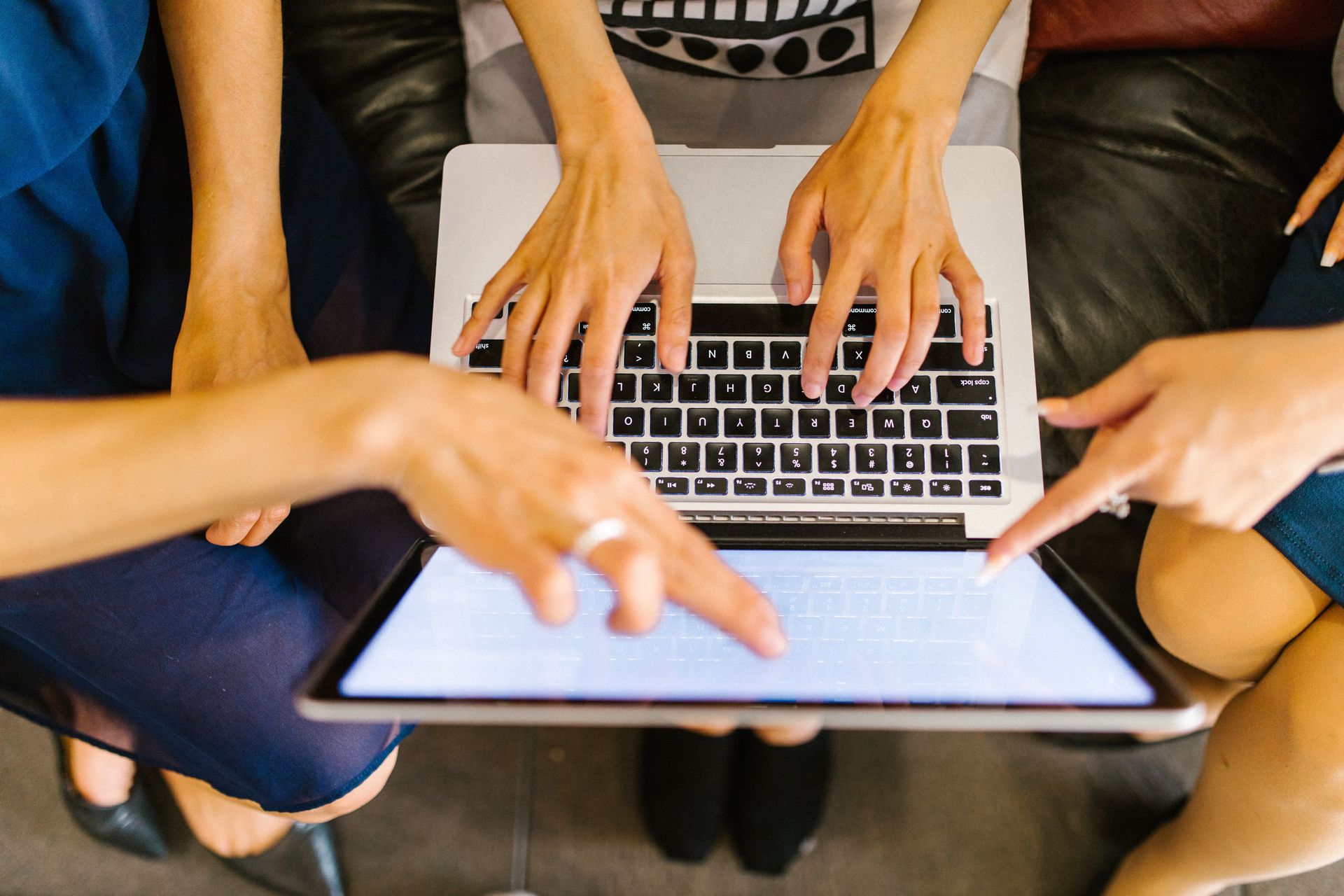 Hands typing on a laptop around a tablet, suggesting a collaborative meeting.