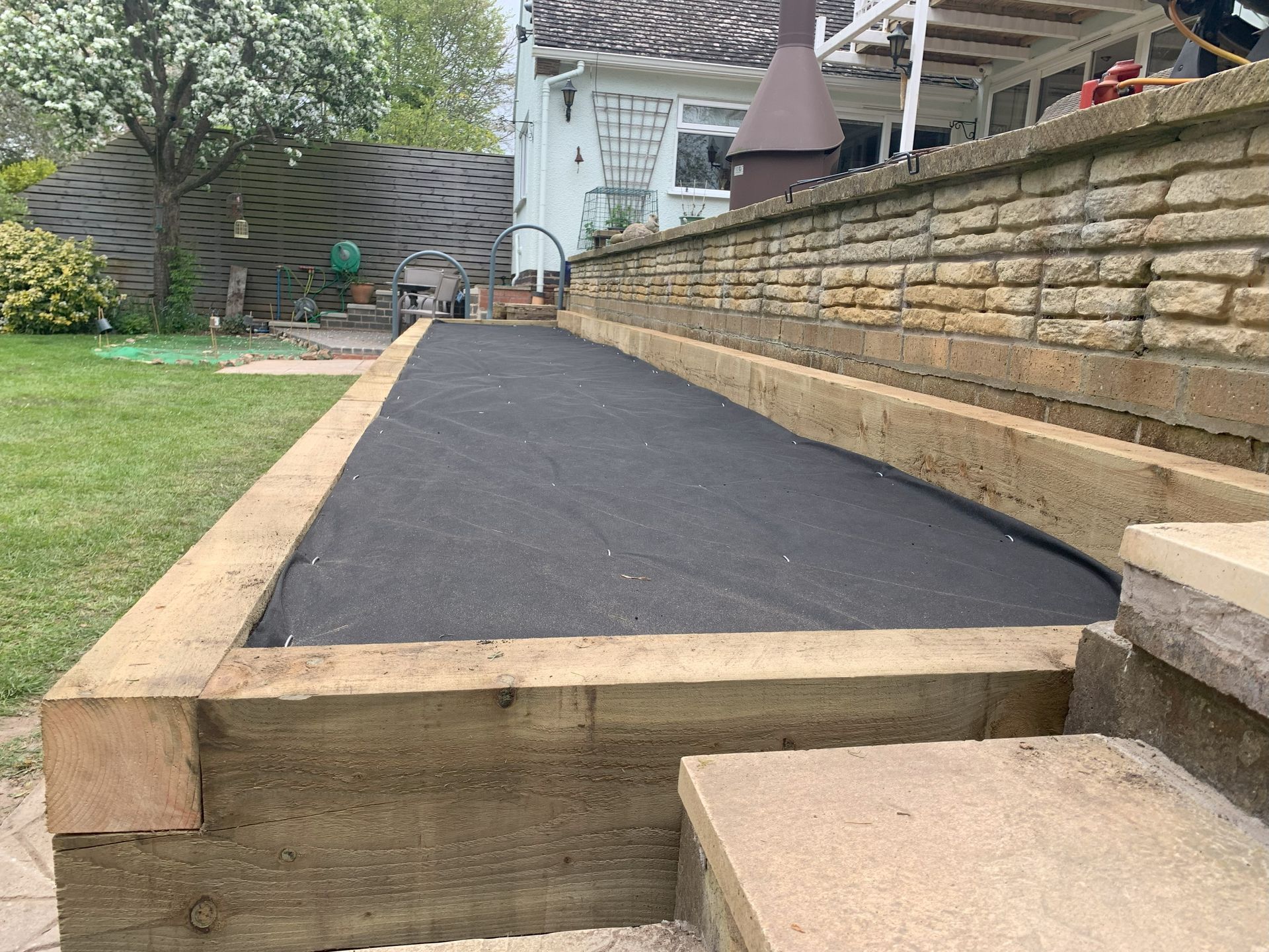 A wooden walkway is being built in a backyard next to a brick wall.