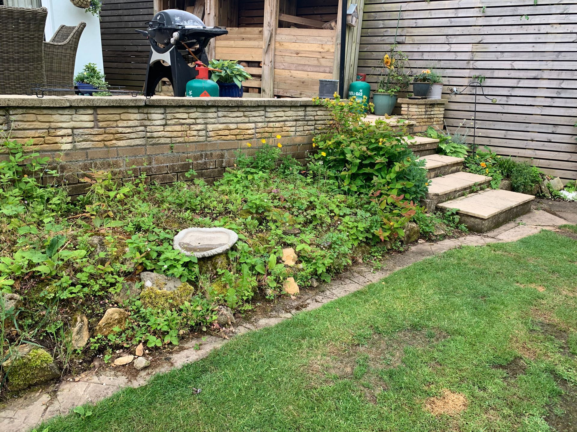 A backyard with a brick wall , steps , plants and a grill.