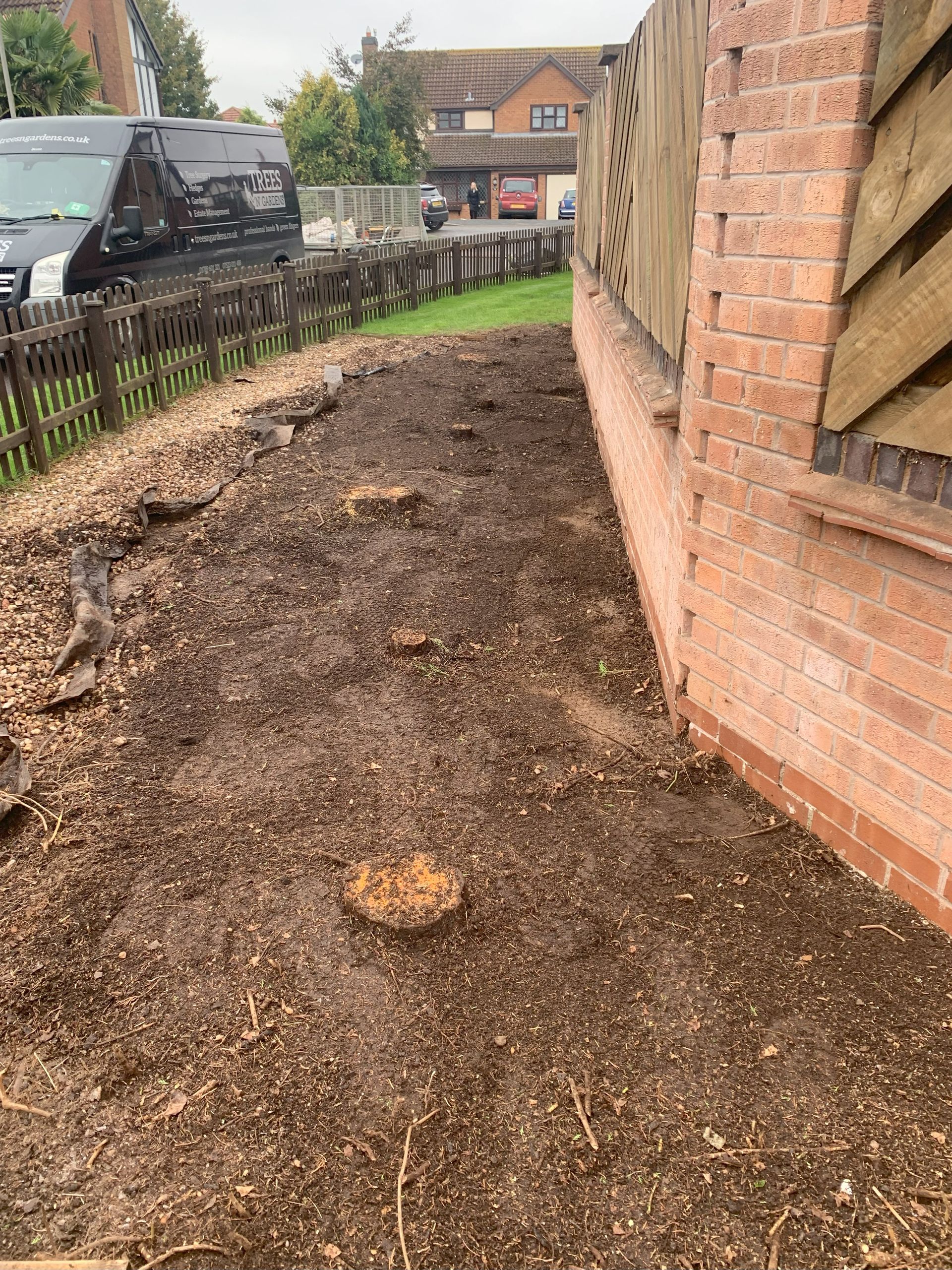 A stump is sitting in the dirt next to a brick wall.