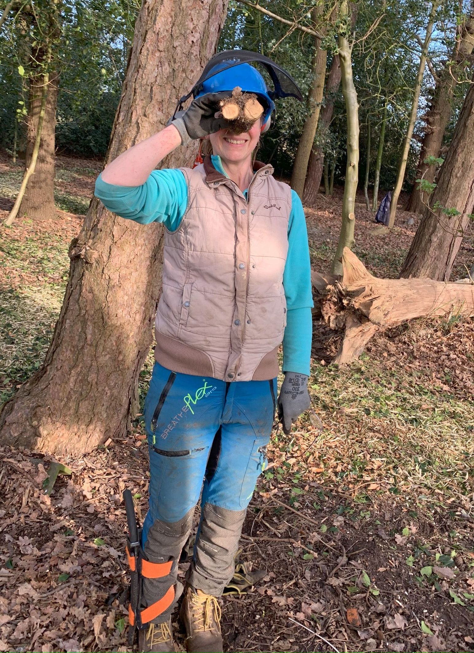 A woman wearing a helmet and sunglasses is standing in the woods.
