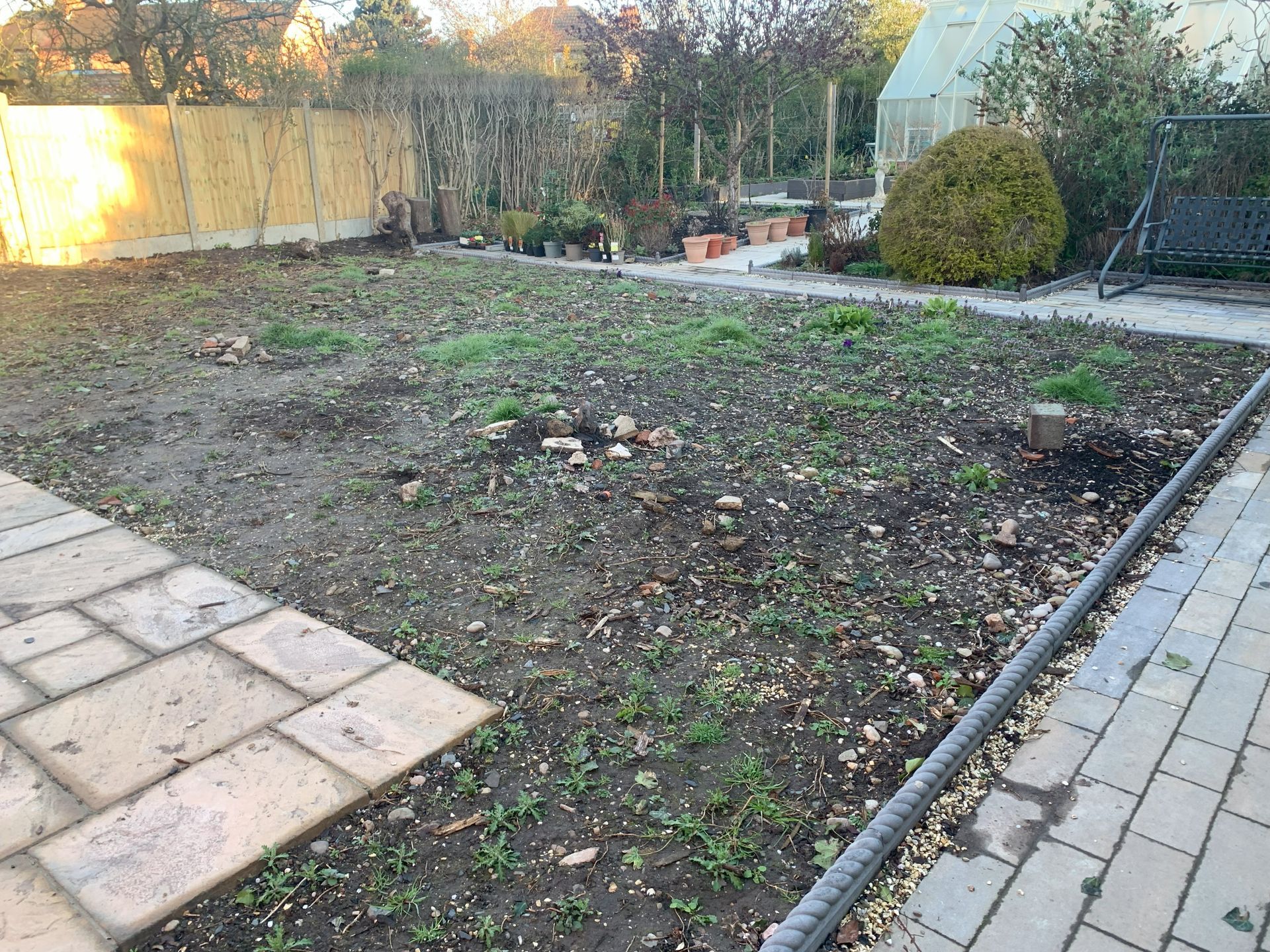 A backyard with a brick walkway and a greenhouse in the background.