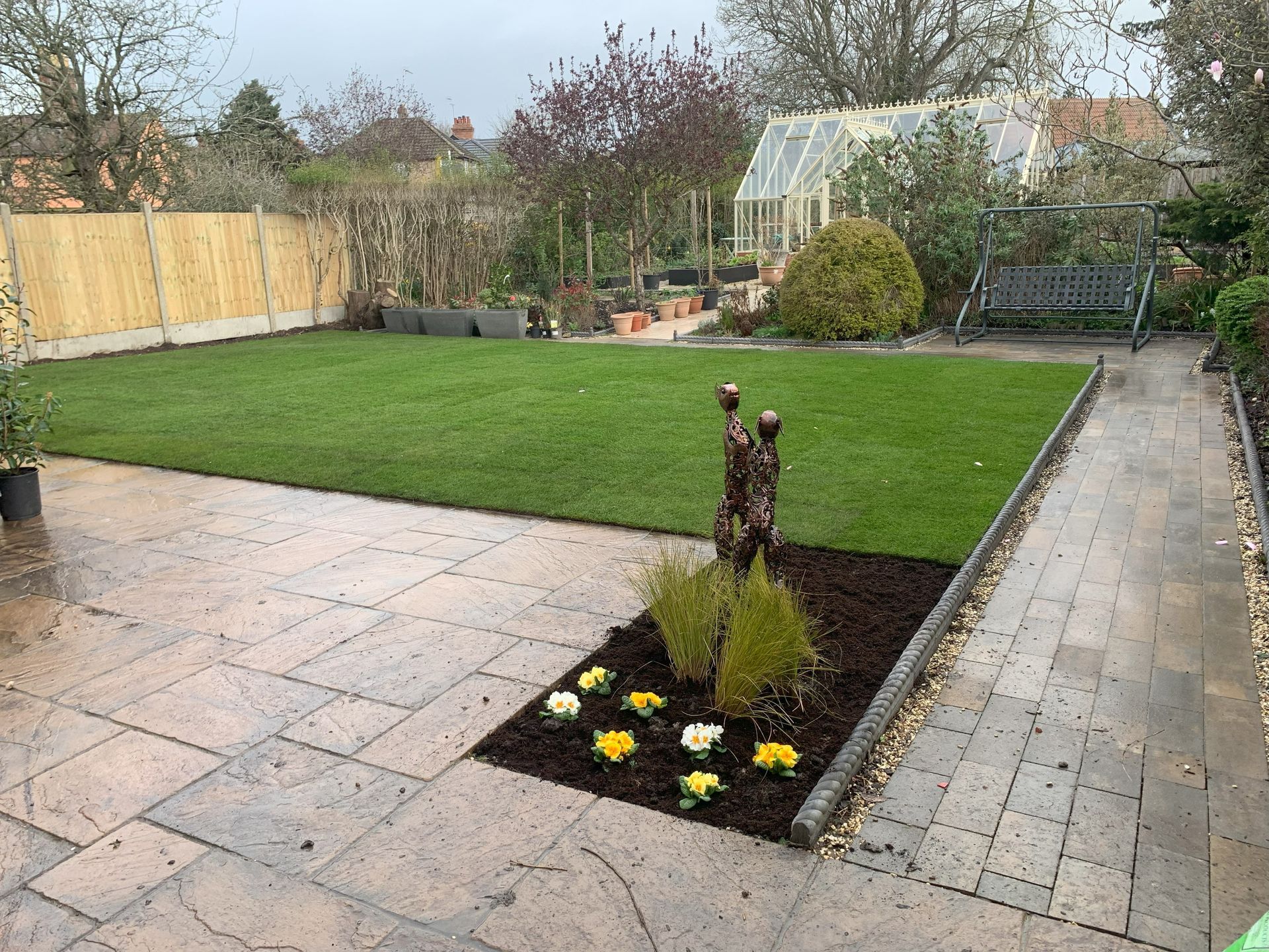 A garden with a patio and a greenhouse in the background.