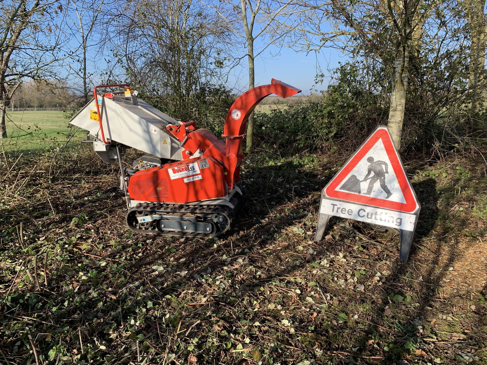 A red machine is sitting next to a sign that says tree cutting.