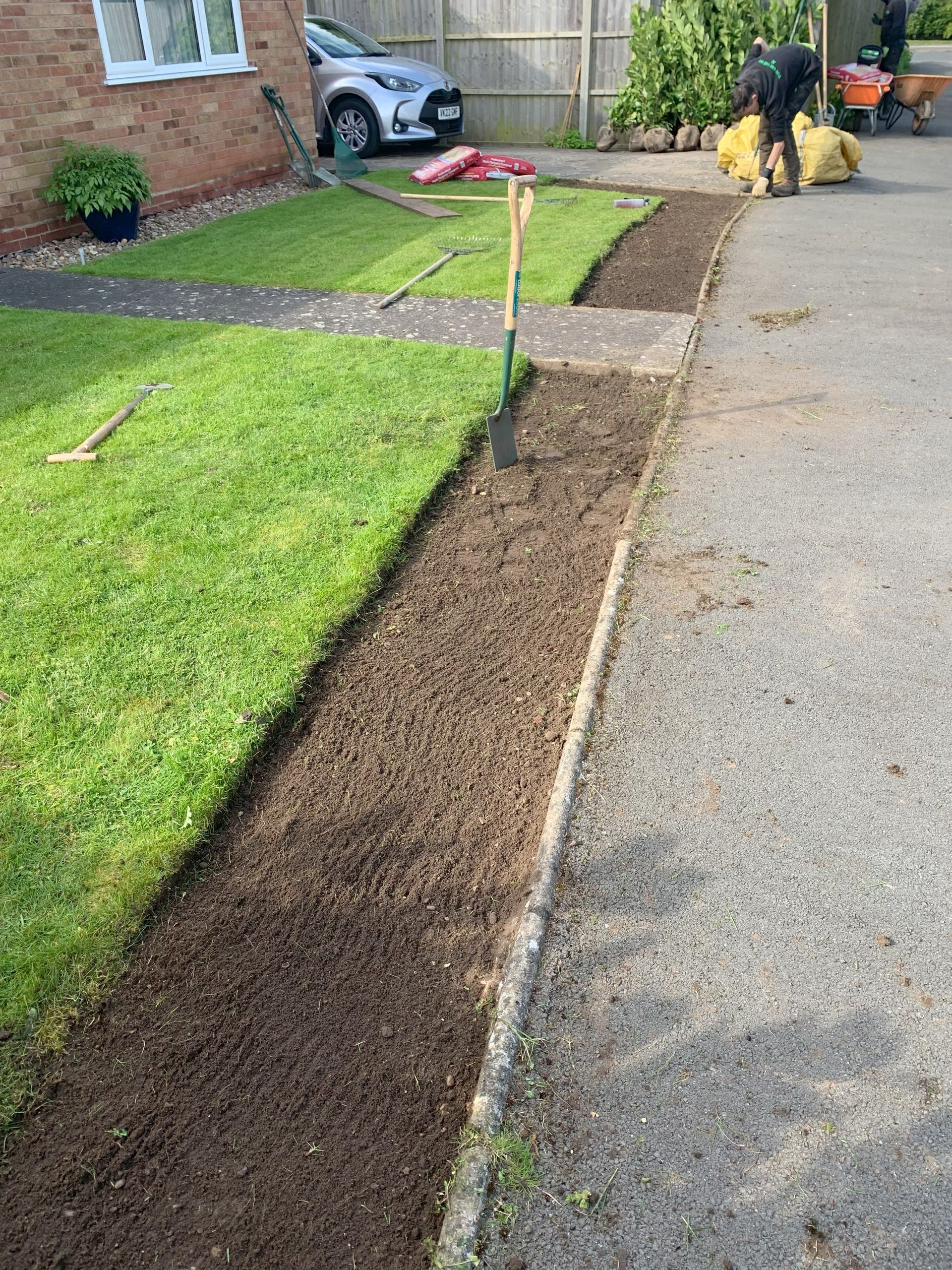 A person is working on a sidewalk next to a lawn.