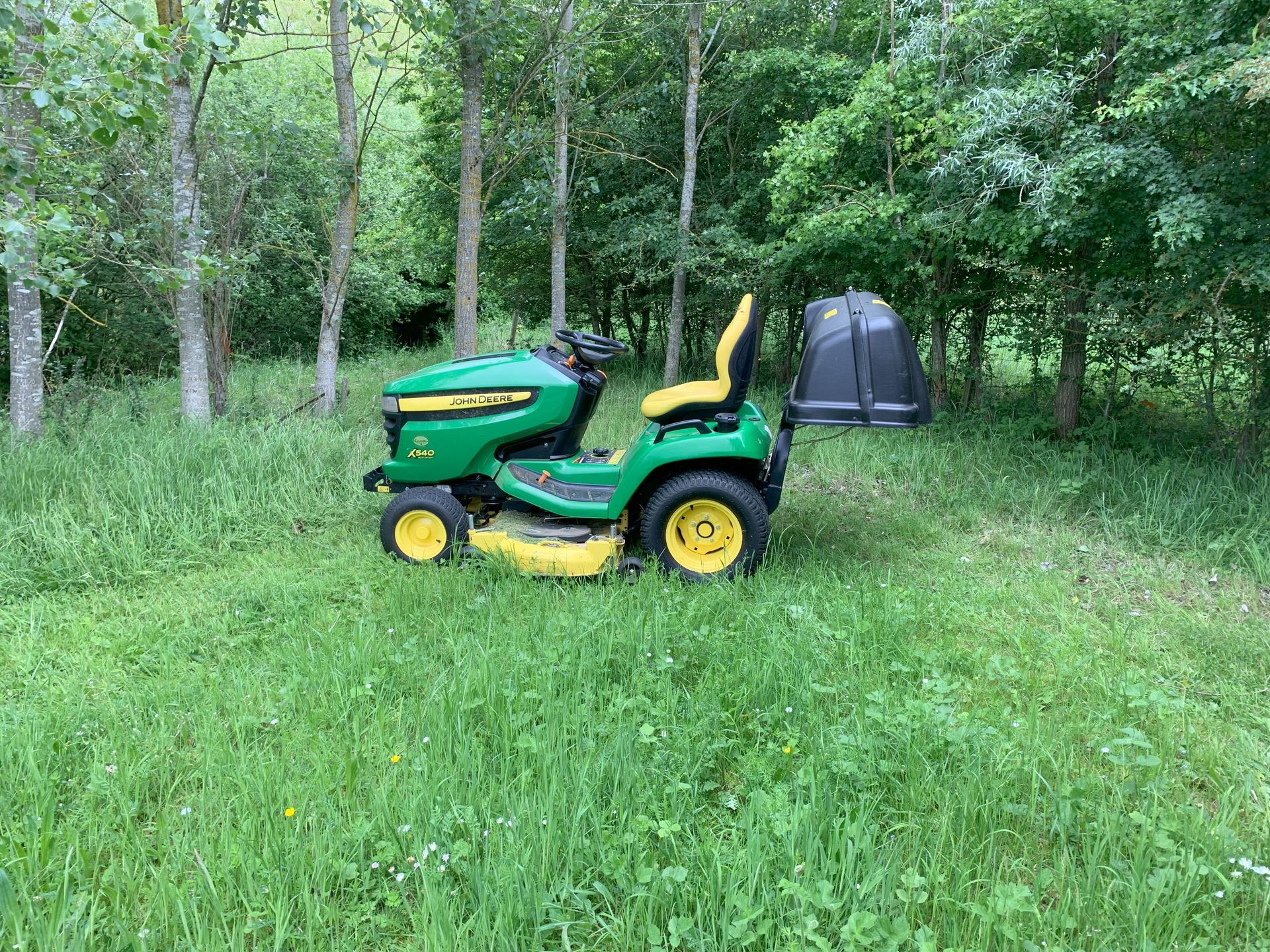 A green and yellow lawn mower is parked in a grassy field.