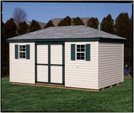 Hip roof shed with beige vinyl siding, 2 white windows with green shutters, green trim, a set of double doors, and a light gray asphalt roof.
