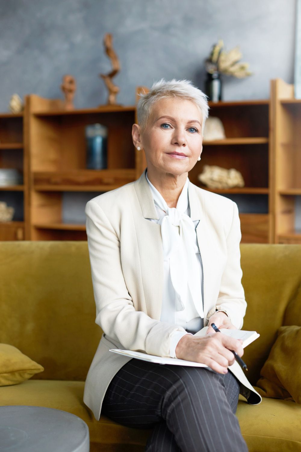 Woman seated on a green sofa in a modern office, holding a notebook with shelves in the background