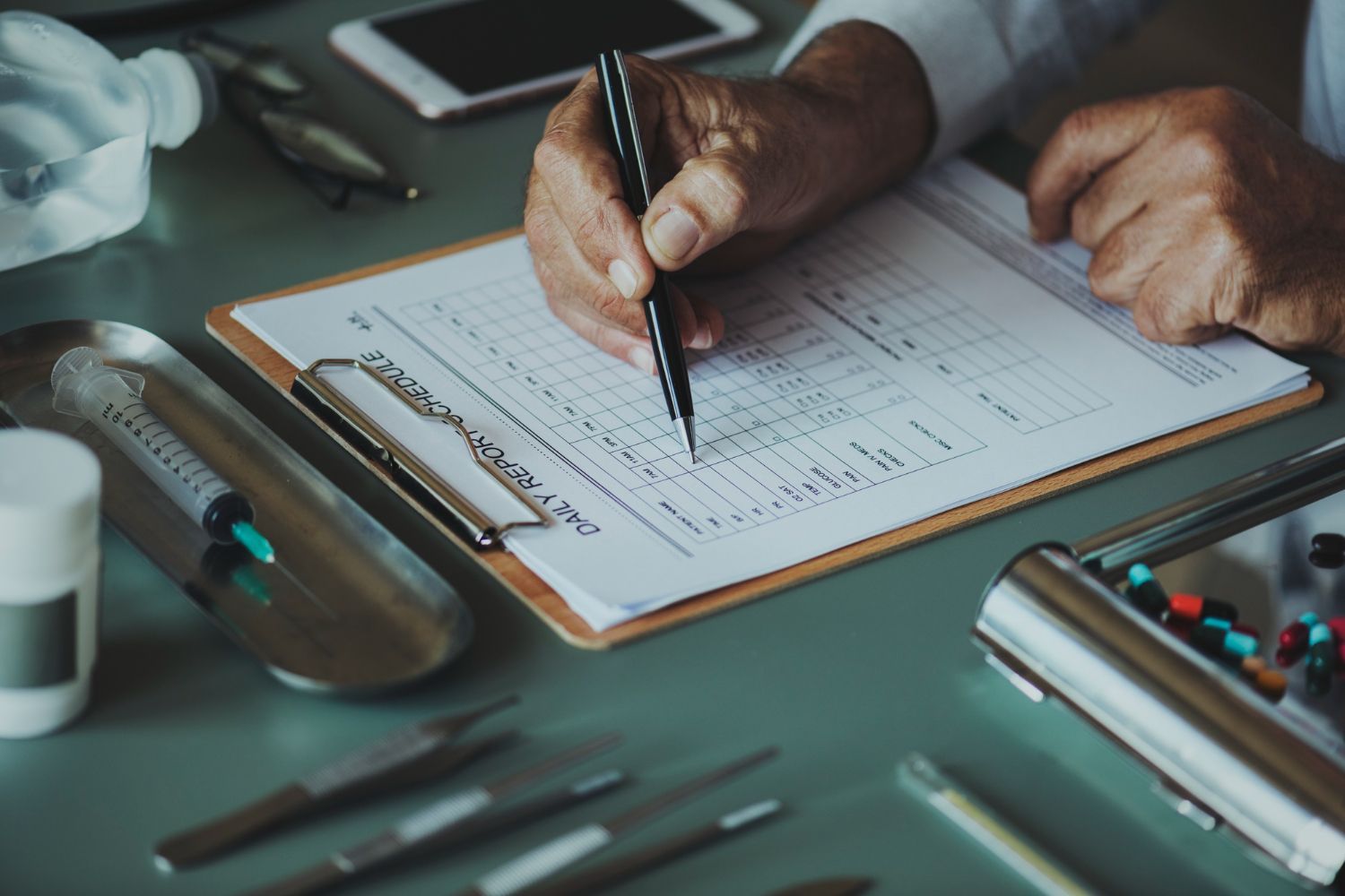Hands holding a pen over a clipboard with a form on a desk, with office supplies nearby.