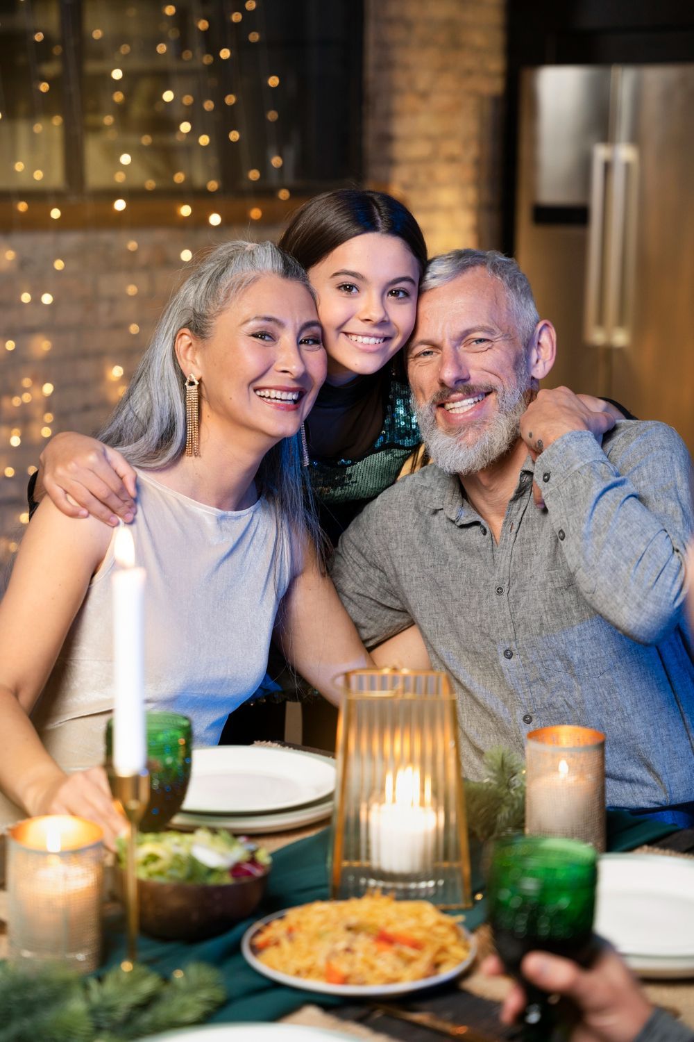 Three people smiling at a candlelit dinner table with drinks and food on a patio