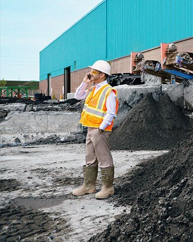 Construction worker in safety vest and hard hat on the phone at a worksite.