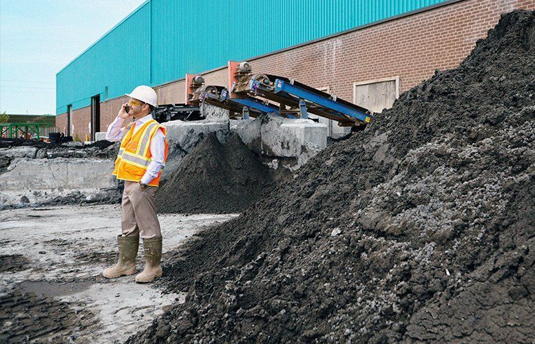 Construction worker in hard hat and safety vest on a job site talking on a cell phone.